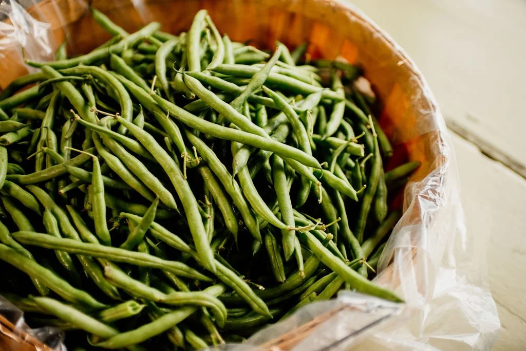 Fresh green beans inside a woven basket lined with plastic.