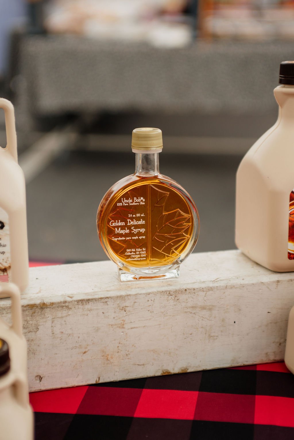 A small, round glass bottle of Uncle Bob's Golden Delicate Maple Syrup with a gold cap, placed on a white wooden surface.