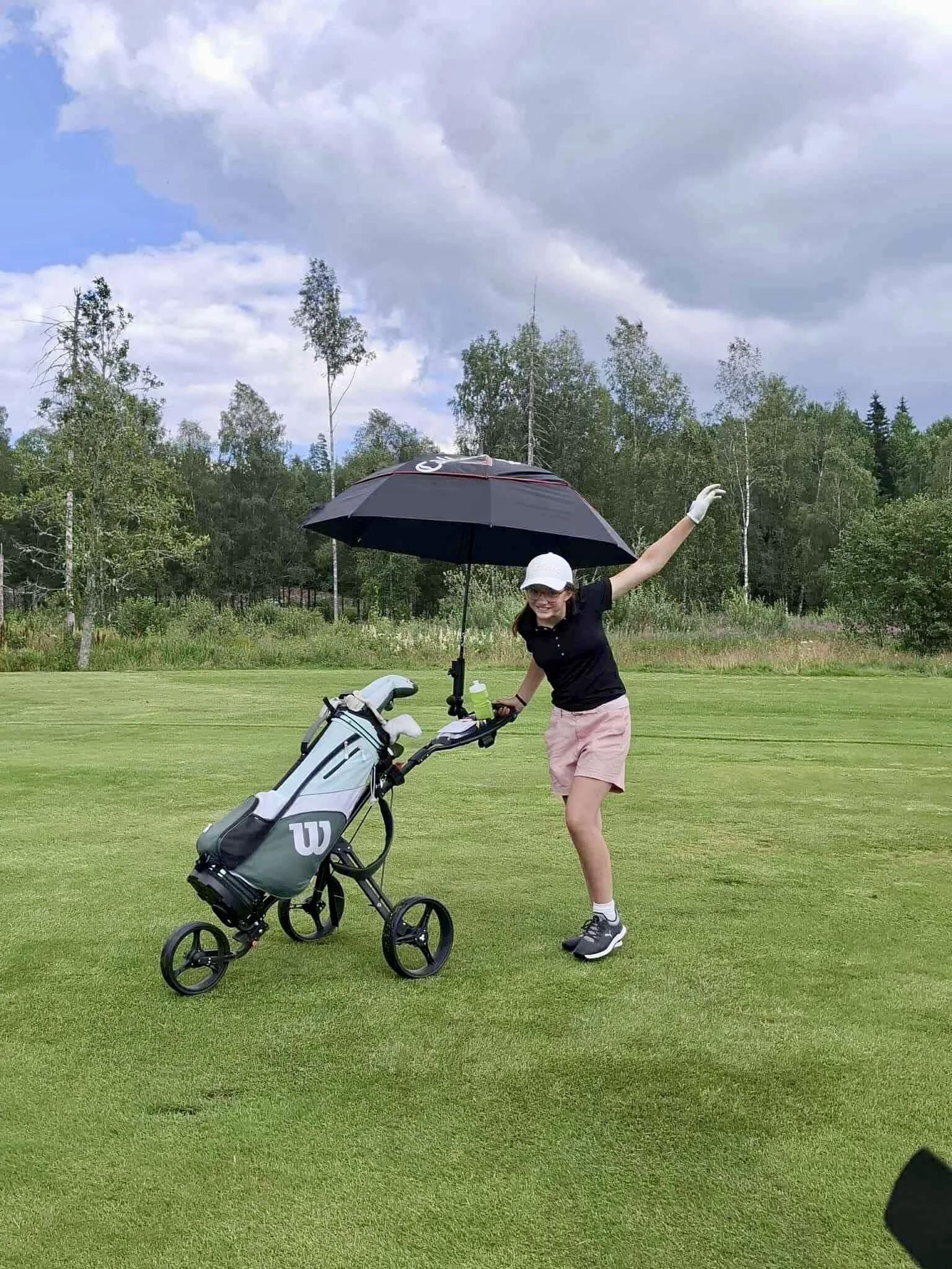 Ung tjej som är glad och går på en golfbana med sin golfvagn