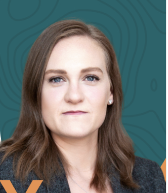 A woman with long, light brown hair and blue eyes, wearing a dark blazer, against a teal background with a subtle pattern.