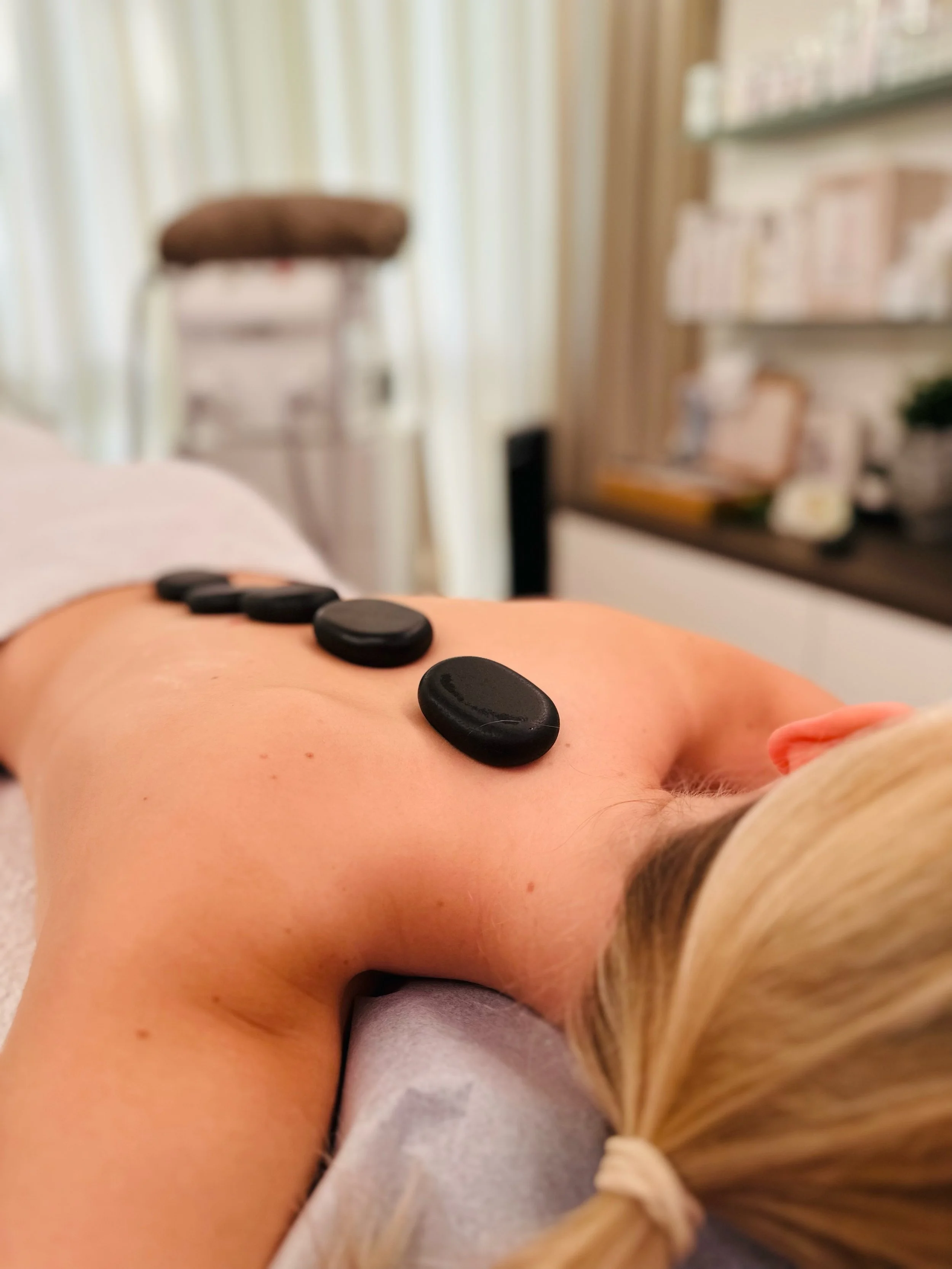 Person bei einer Hot-Stone-Massage mit schwarzen Steinen auf dem Rücken.
