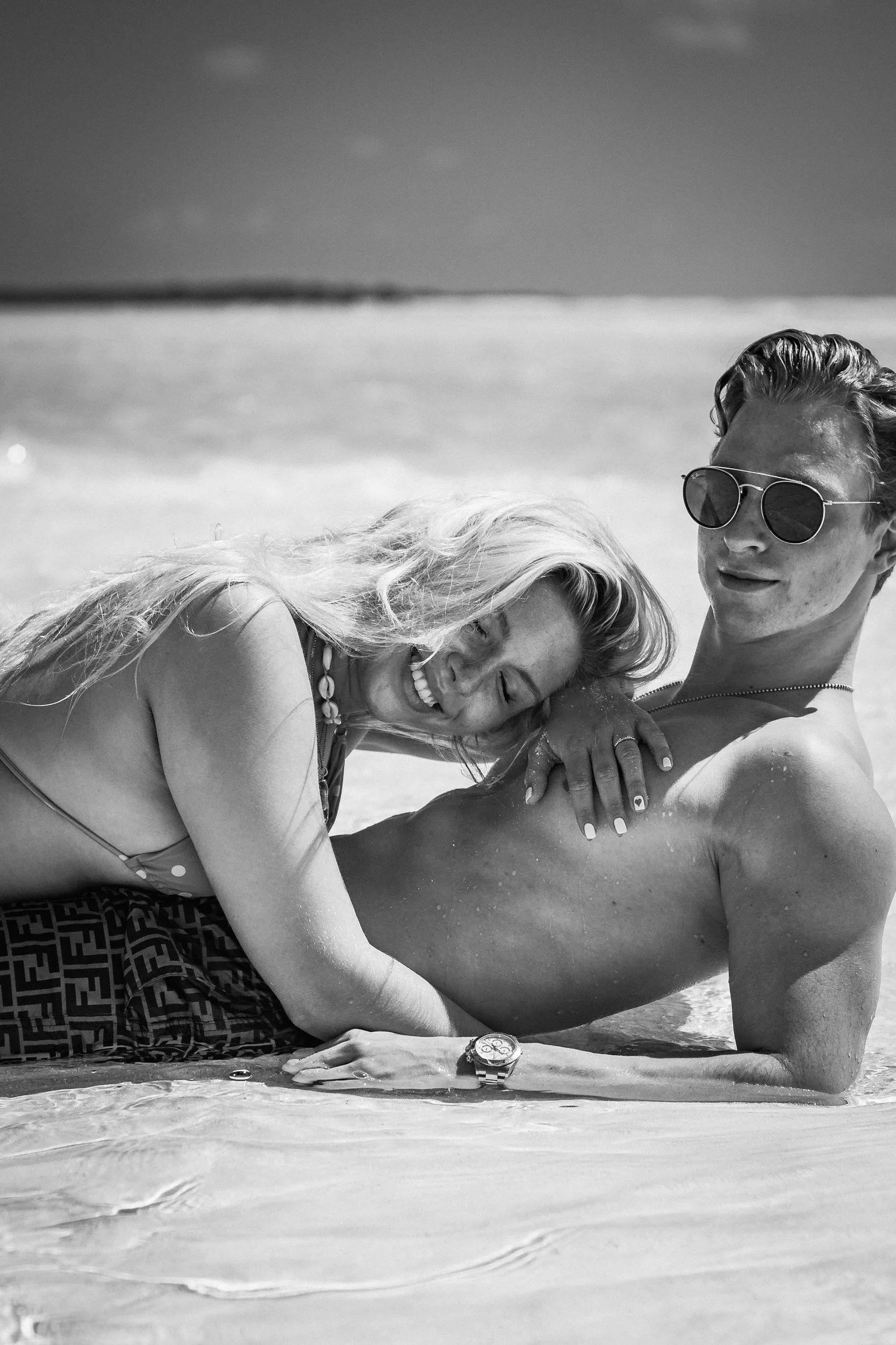 A couple lying on the beach, smiling and relaxing in the sun, with the ocean in the background.