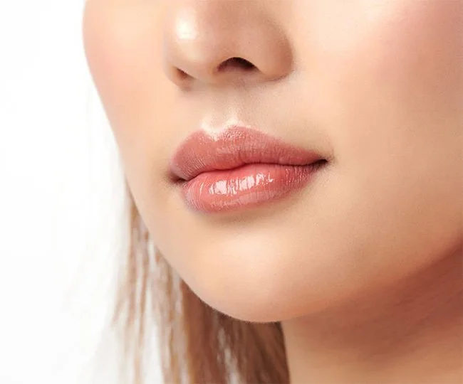 Close-up of a woman's lips with glossy pink lipstick and smooth skin.