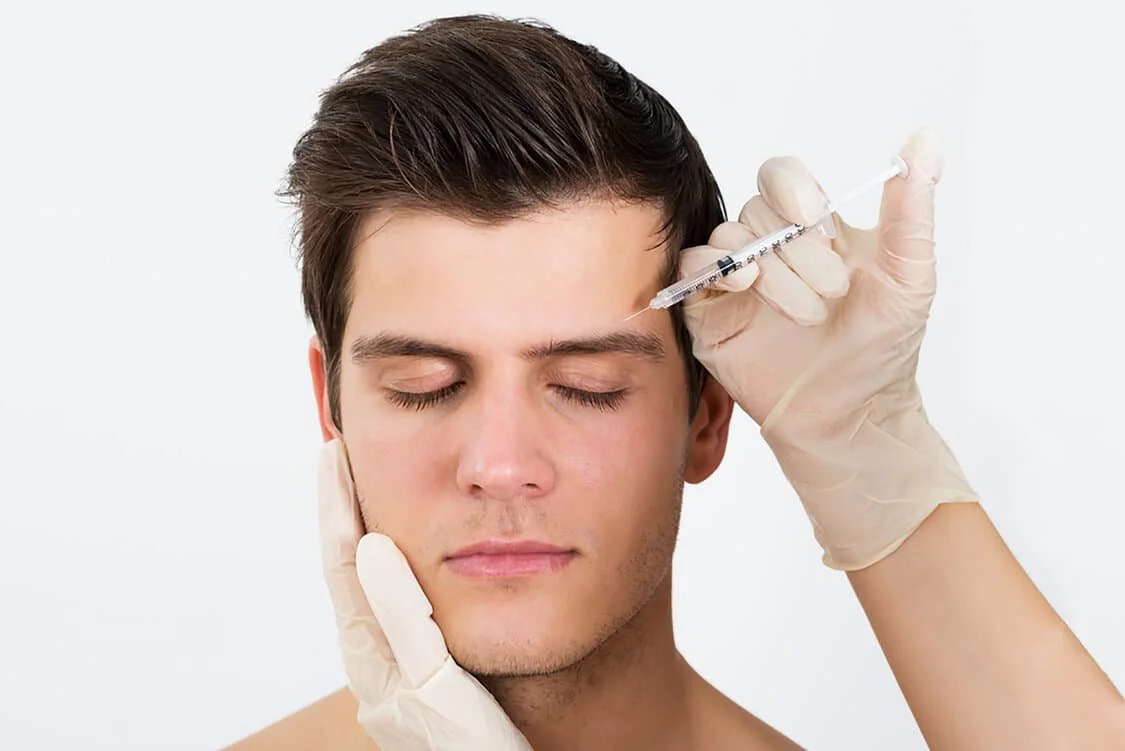 A man receiving a botox cosmetic injection into his forehead from a professional aesthetician wearing gloves.