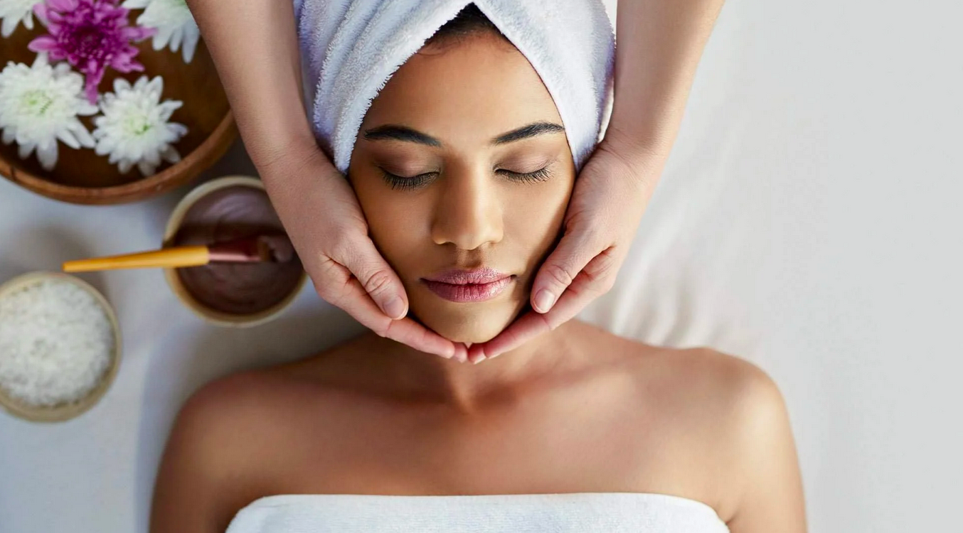 Woman receiving a facial massage with spa products nearby.