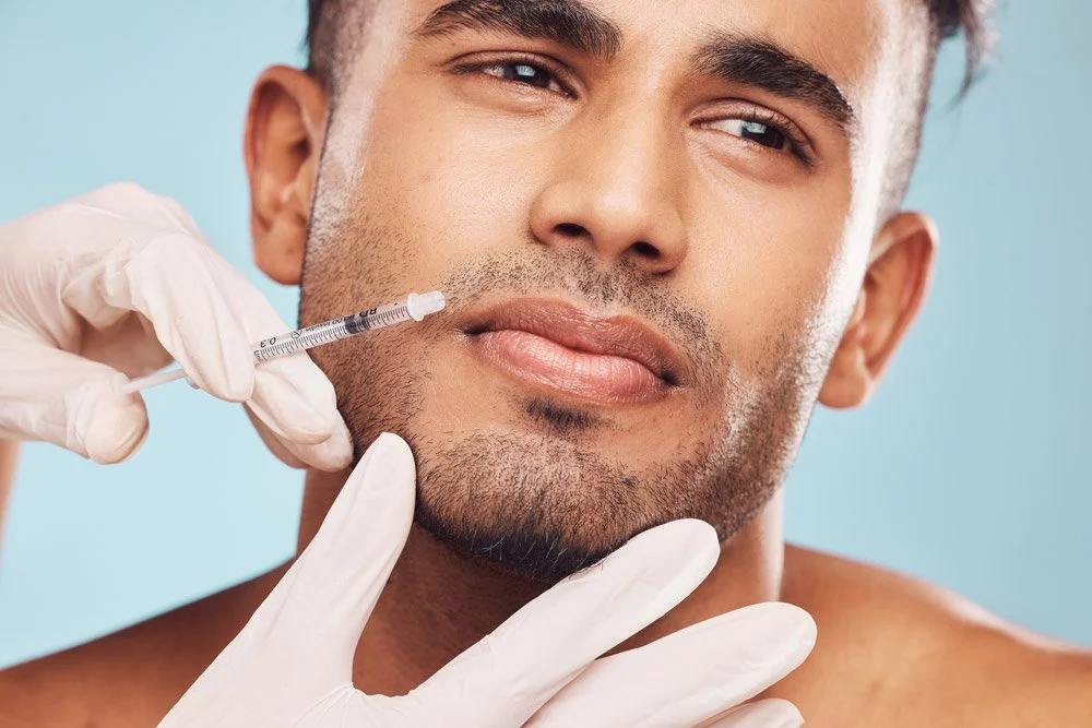 A man receiving a botox cosmetic injection into his forehead from a professional aesthetician wearing gloves.