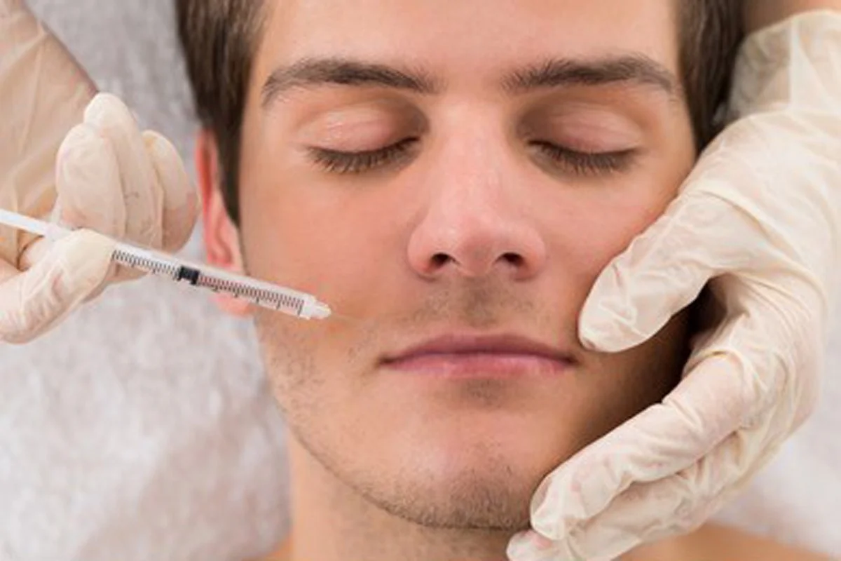 A man receiving a botox cosmetic injection into his forehead from a professional aesthetician wearing gloves.