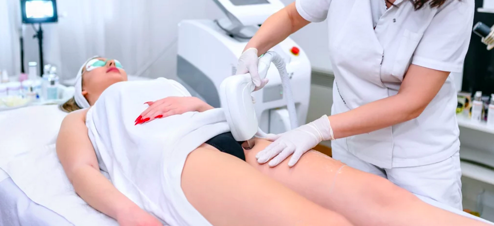 Medical professional performs a laser treatment on a woman lying on a medical bed in a clinical setting.