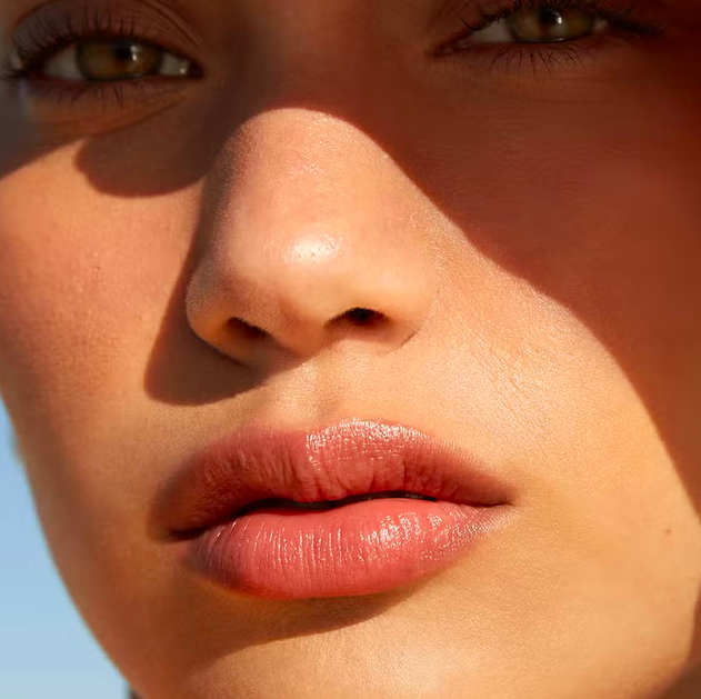 Close-up of a woman's face showing her eyes, nose, and lips with natural makeup and sunlight highlighting her features.