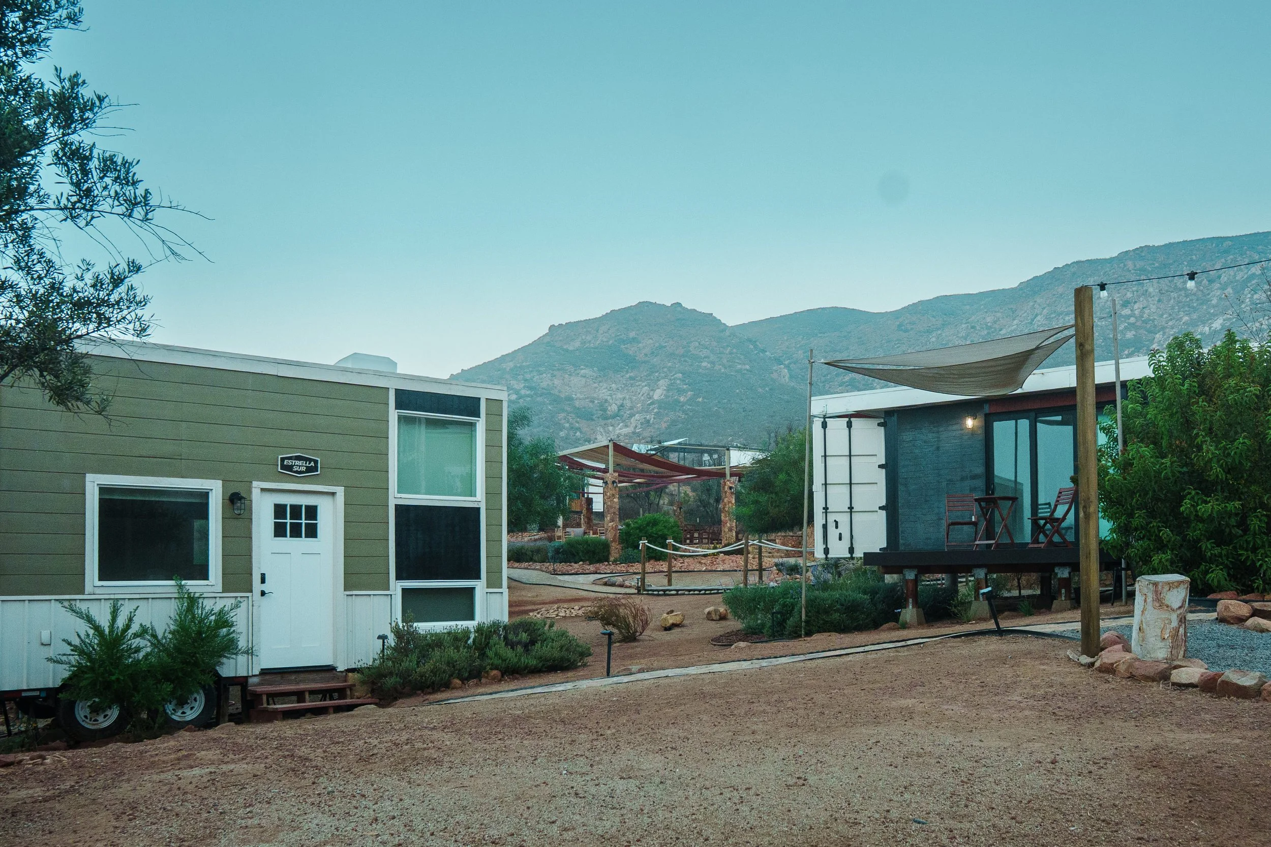 View of modern houses with mountain backdrop and a clear sky, including an outdoor seating area with chairs and string lights.