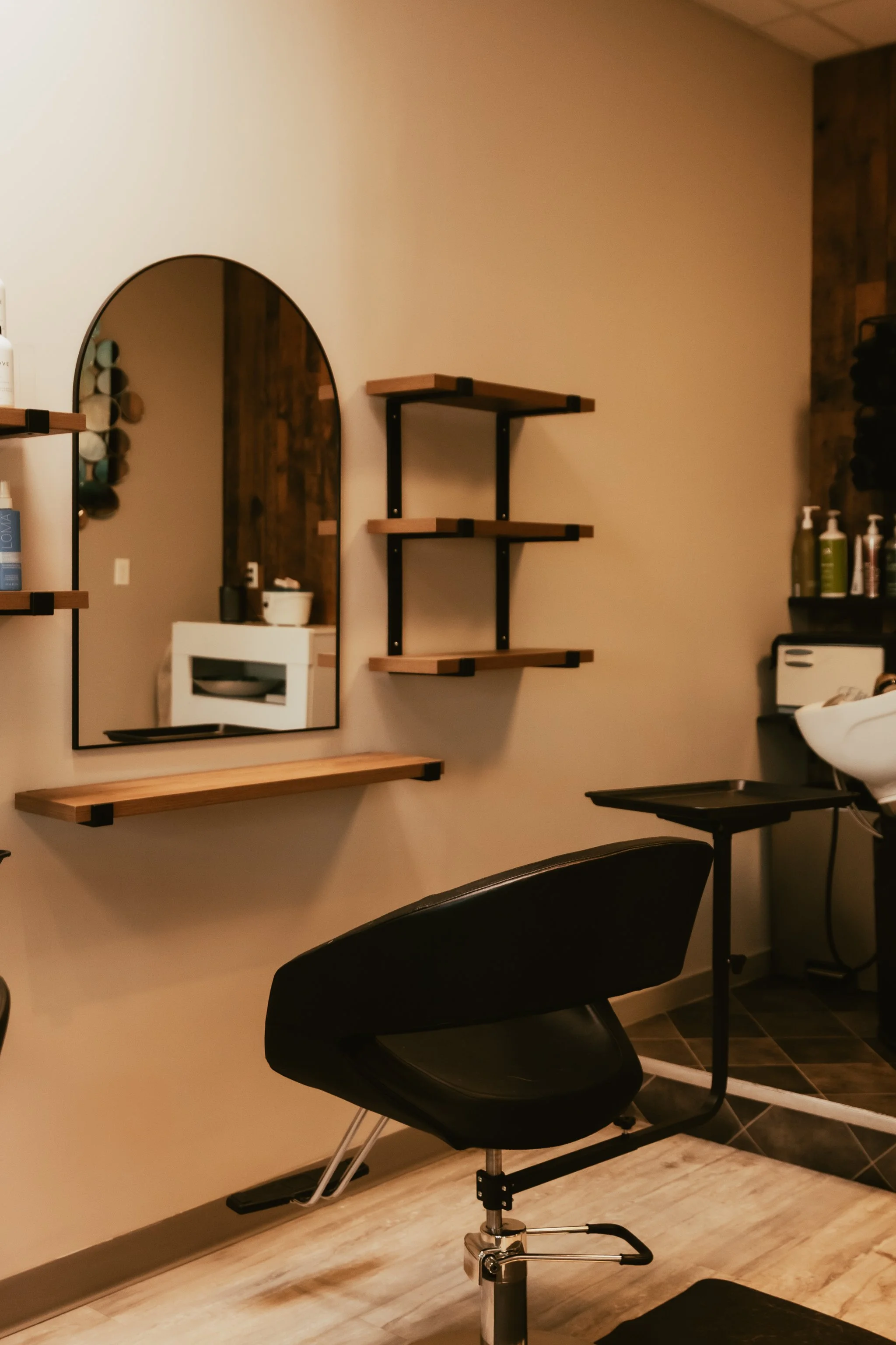 Salon interior with a styling chair, wooden wall, potted plants, wall shelf, and shelves with hair products.