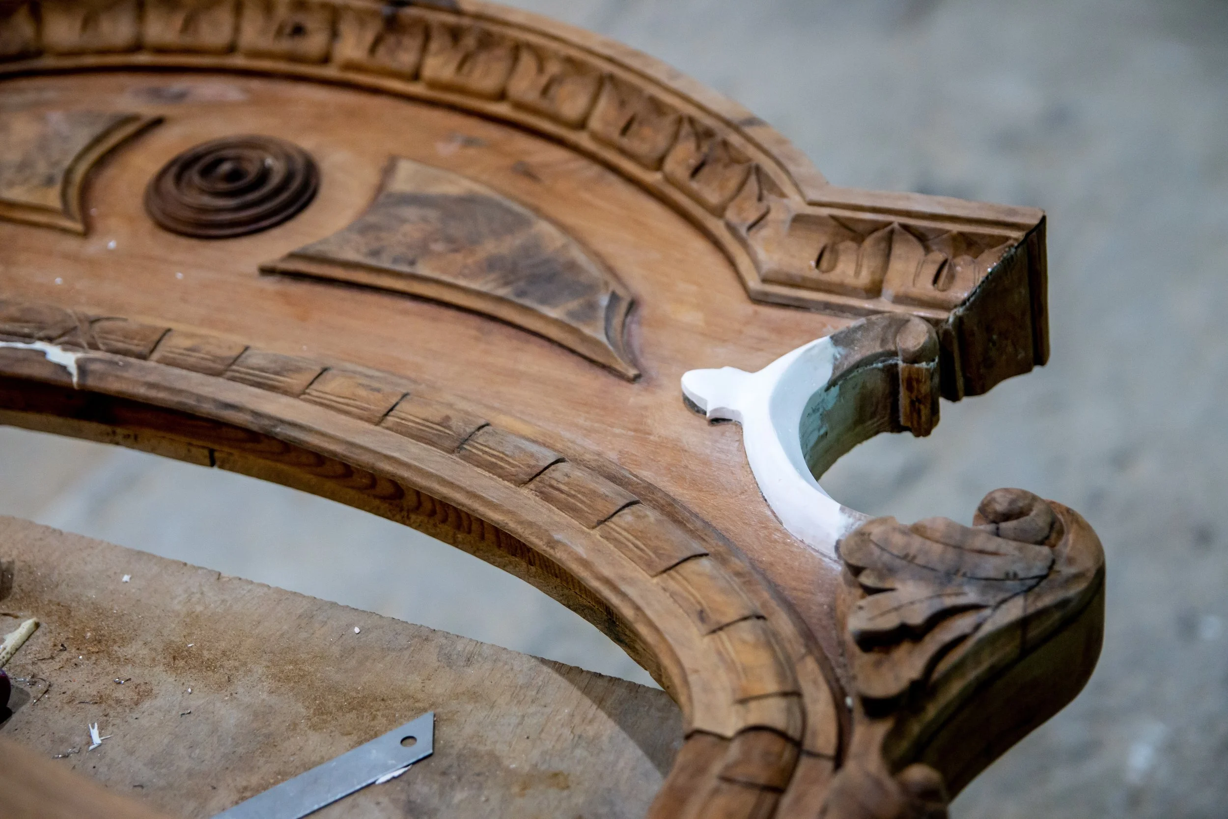 Close-up of an ornately carved wooden piece, likely a part of furniture or architectural detail, with intricate designs and a white painted section.