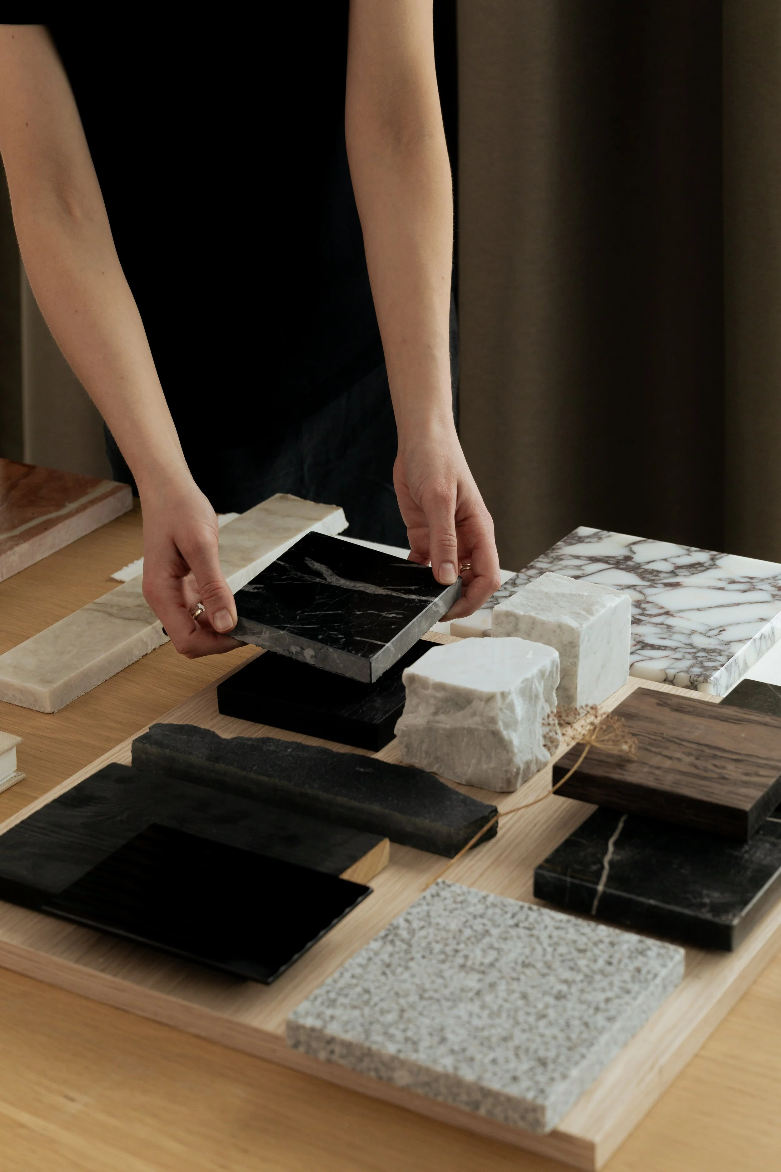 Person arranging various marble and stone tiles on a wooden table.