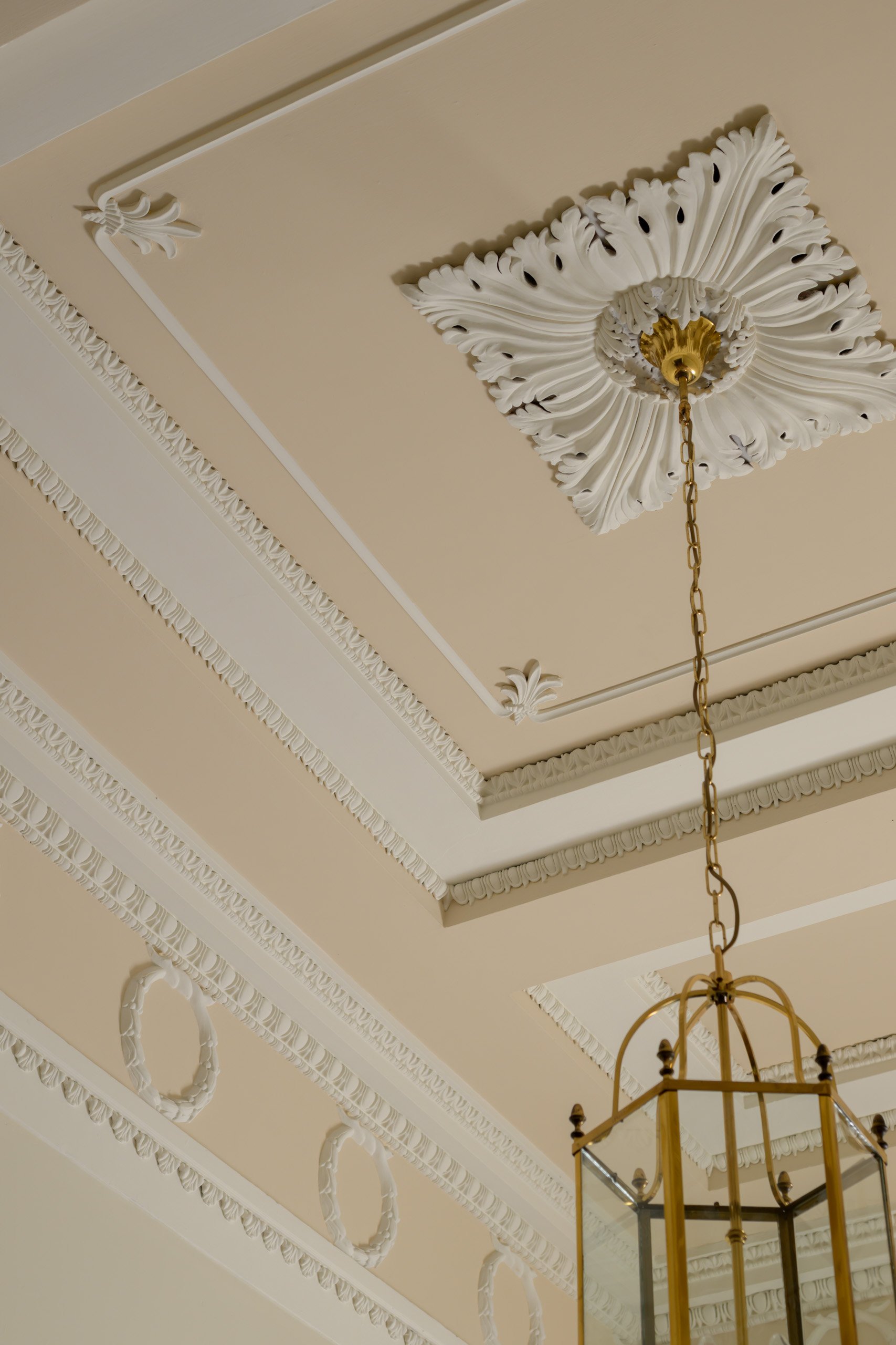 Close-up of a white decorative fireplace mantel with ornate columns and detailed carvings, including a circular emblem with a candle and floral motifs.