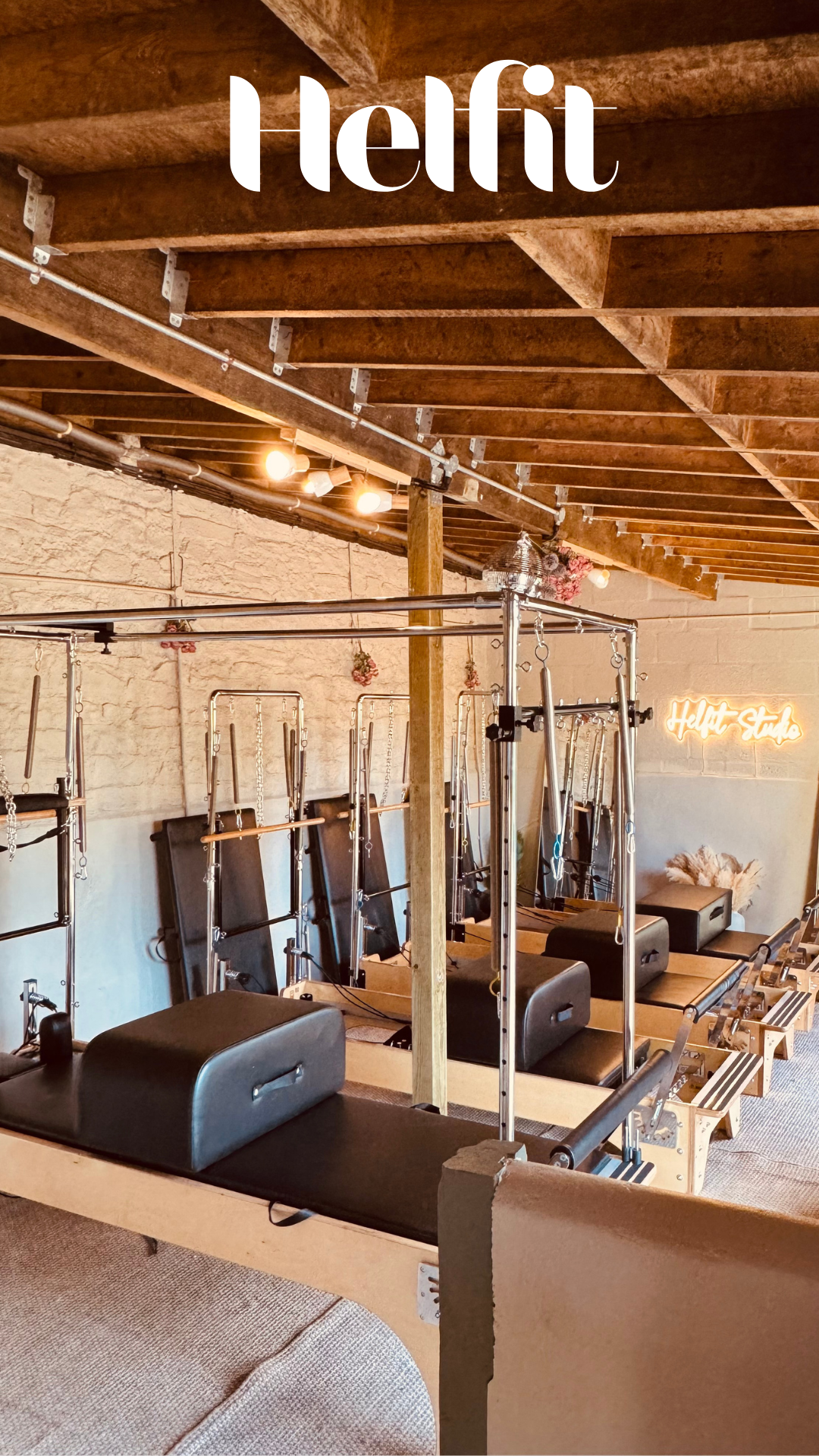 Interior of a Pilates studio with reformer machines, a brick wall, and a neon sign that says 'Helft Studio'.
