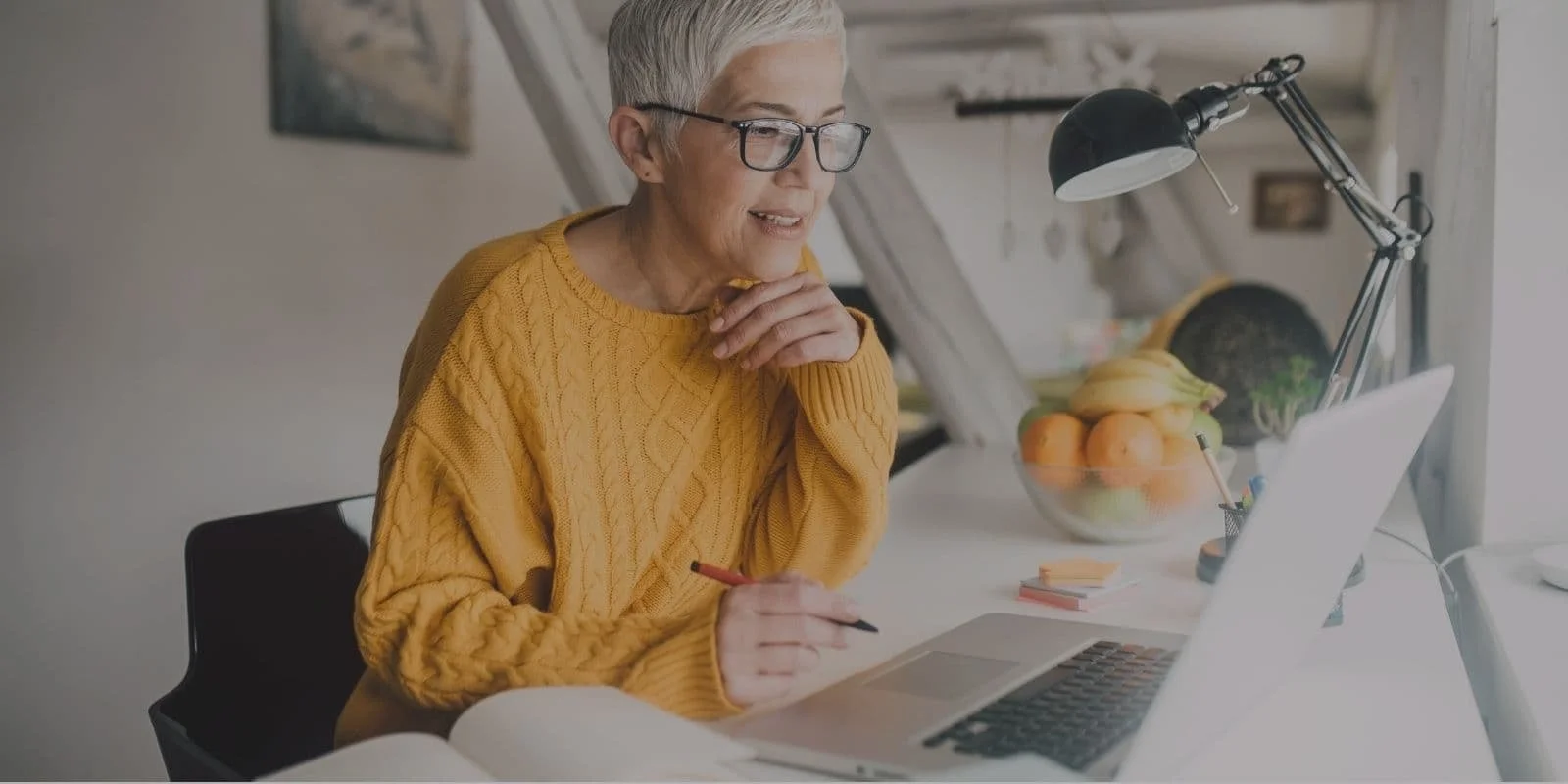 Smiling woman with glasses working on a laptop at a bright office table
