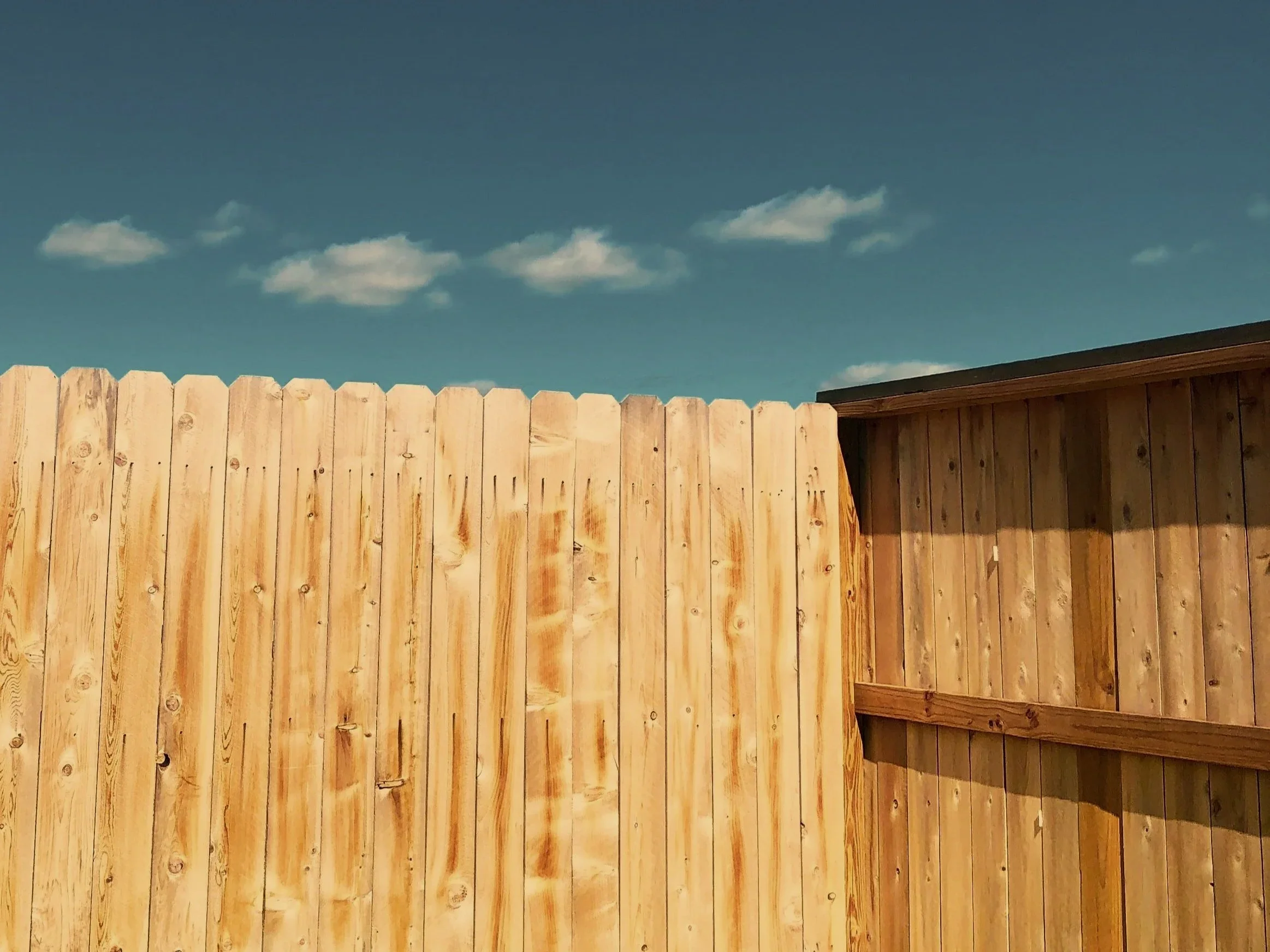 Wooden fence under a blue sky with some scattered white clouds.