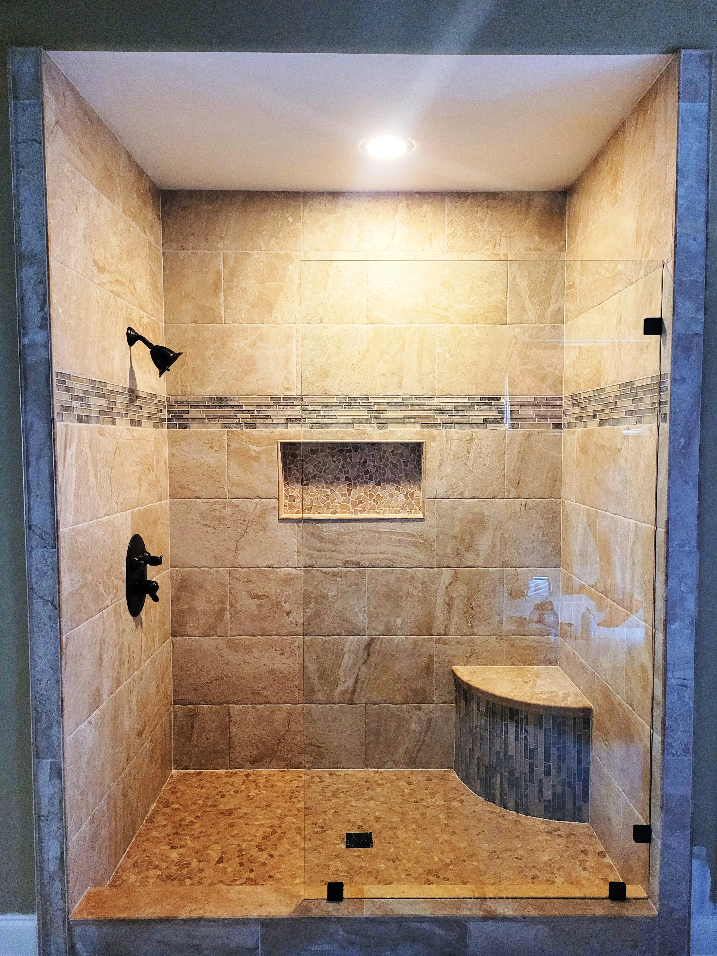 A tiled walk-in shower with a bench, built-in niche, and two black shower fixtures, enclosed by a glass door.