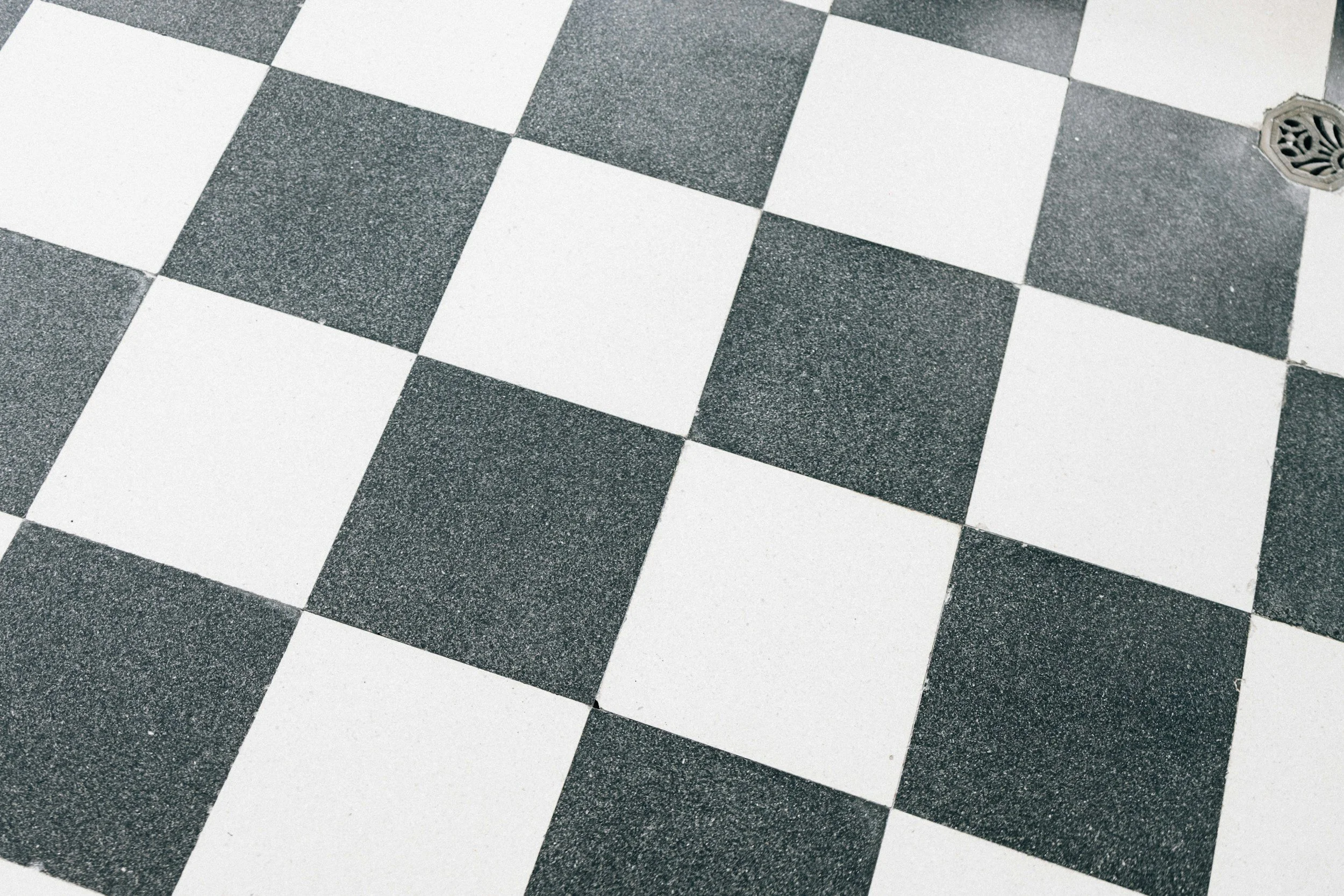 Close-up of black and white checkered tile flooring with a drain cover in the upper right corner.