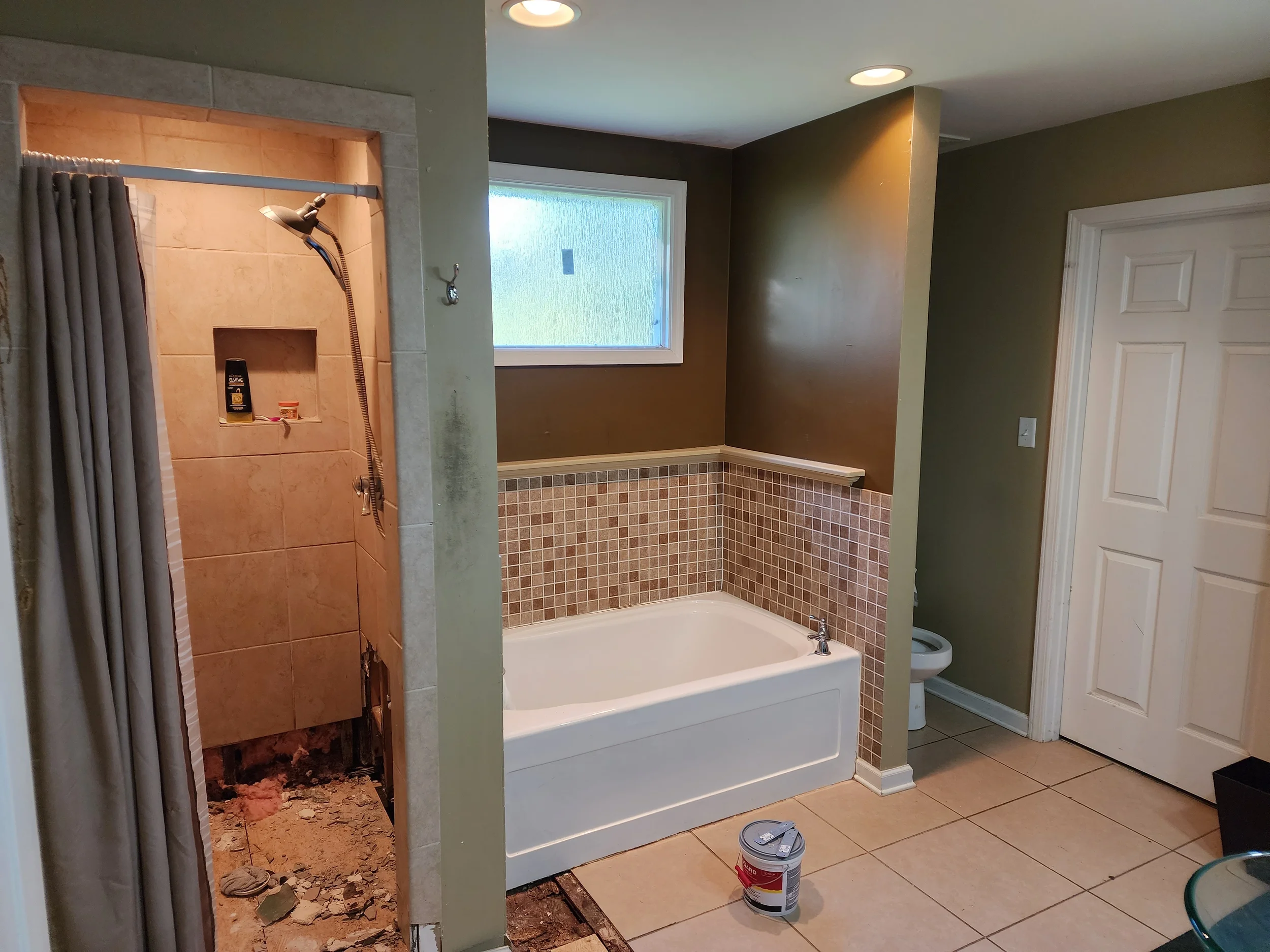 Bathroom with shower stall and bathtub, some wall tiles partially removed, construction materials, and tools visible.