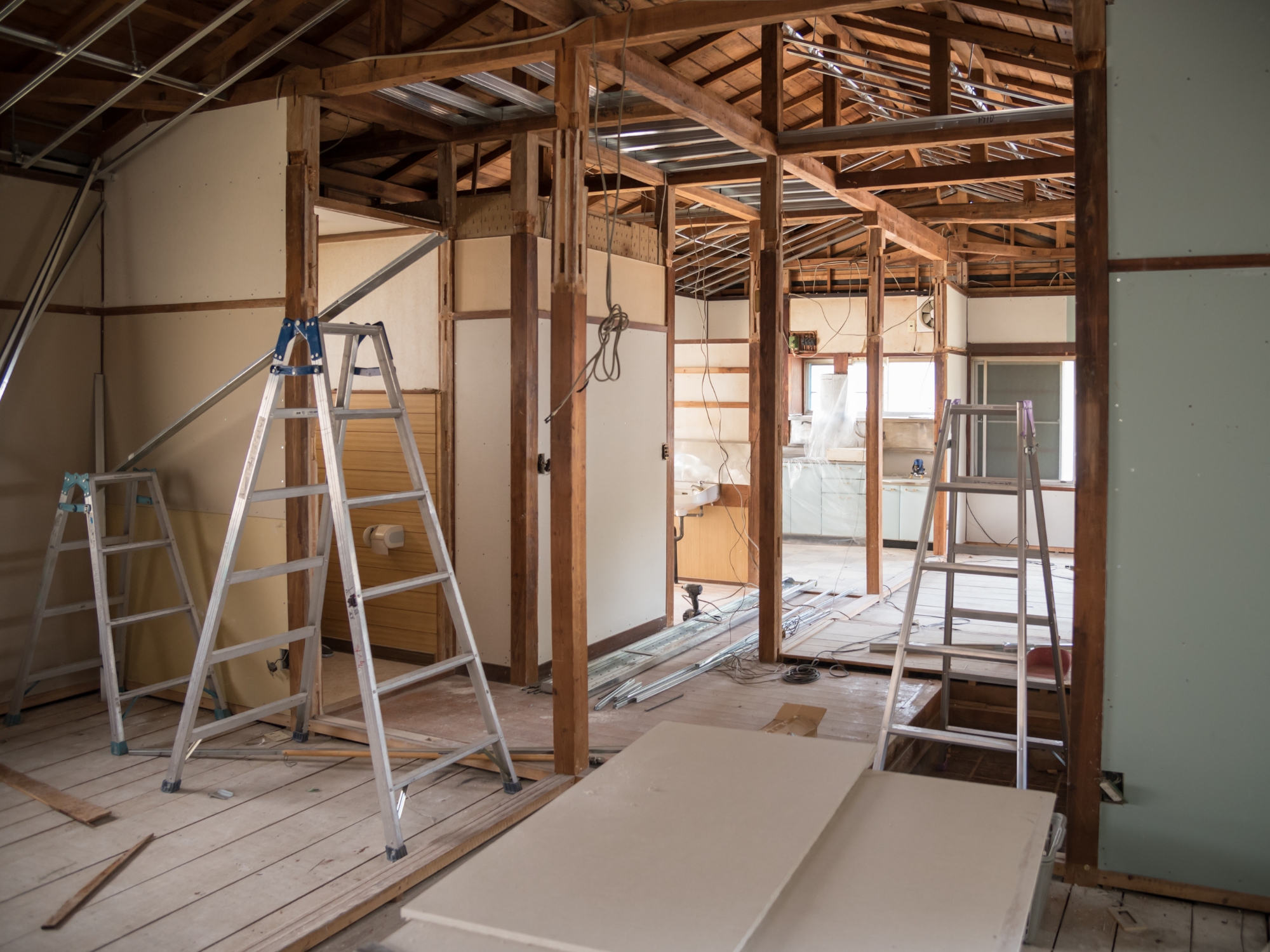 Interior of a house under renovation showing exposed wooden framing, ladders, and construction materials.