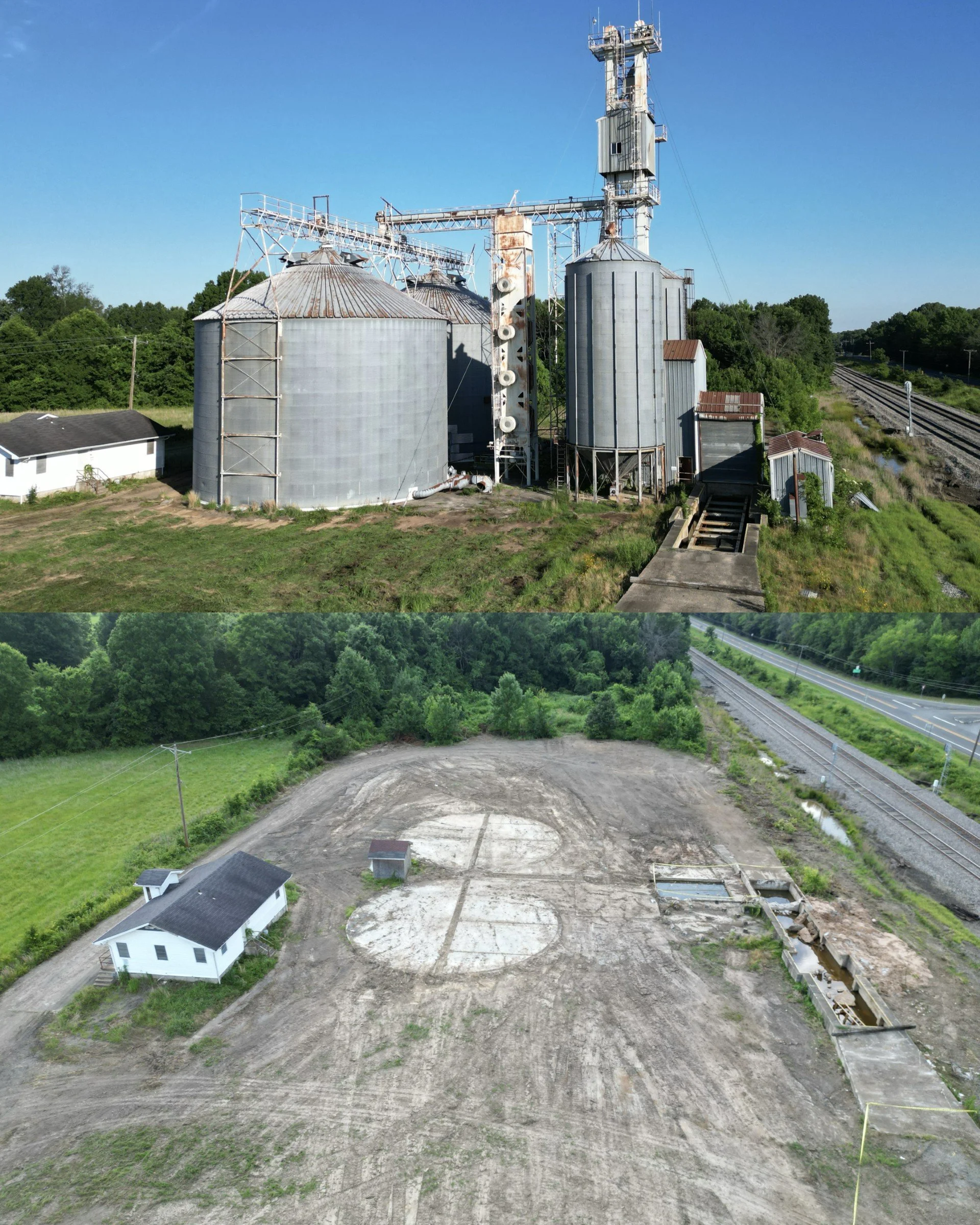 Aerial view of an industrial site next to train tracks with trees and green vegetation in the background, and a partially cleared construction area in the foreground.