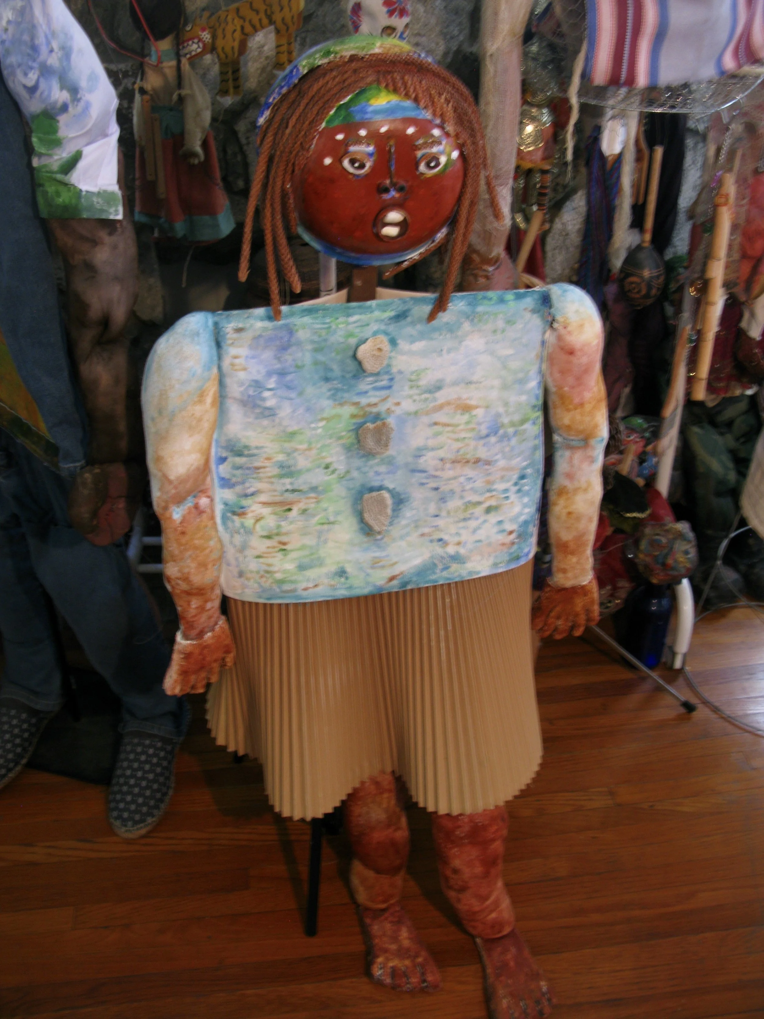 Climate Refugee-Sister. Bamboo plate, acrylic paint, papièr maché, poly-fill, shells, seeds, dried plants, canvas material, stretch fabric, gesso, cheese cloth. h3'10'w1'9'