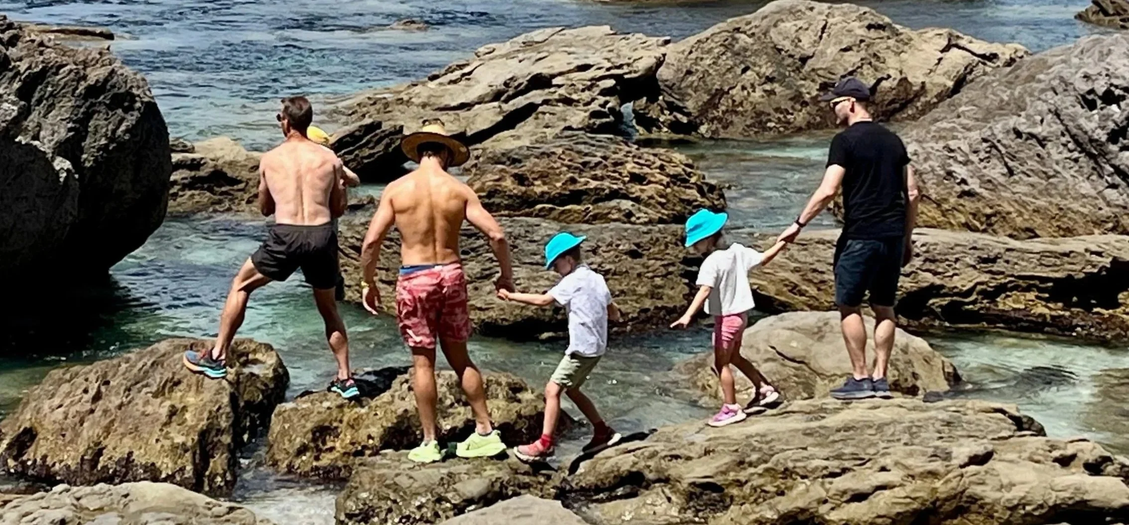Two adults and two children exploring rock pools on a New Zealand coastline