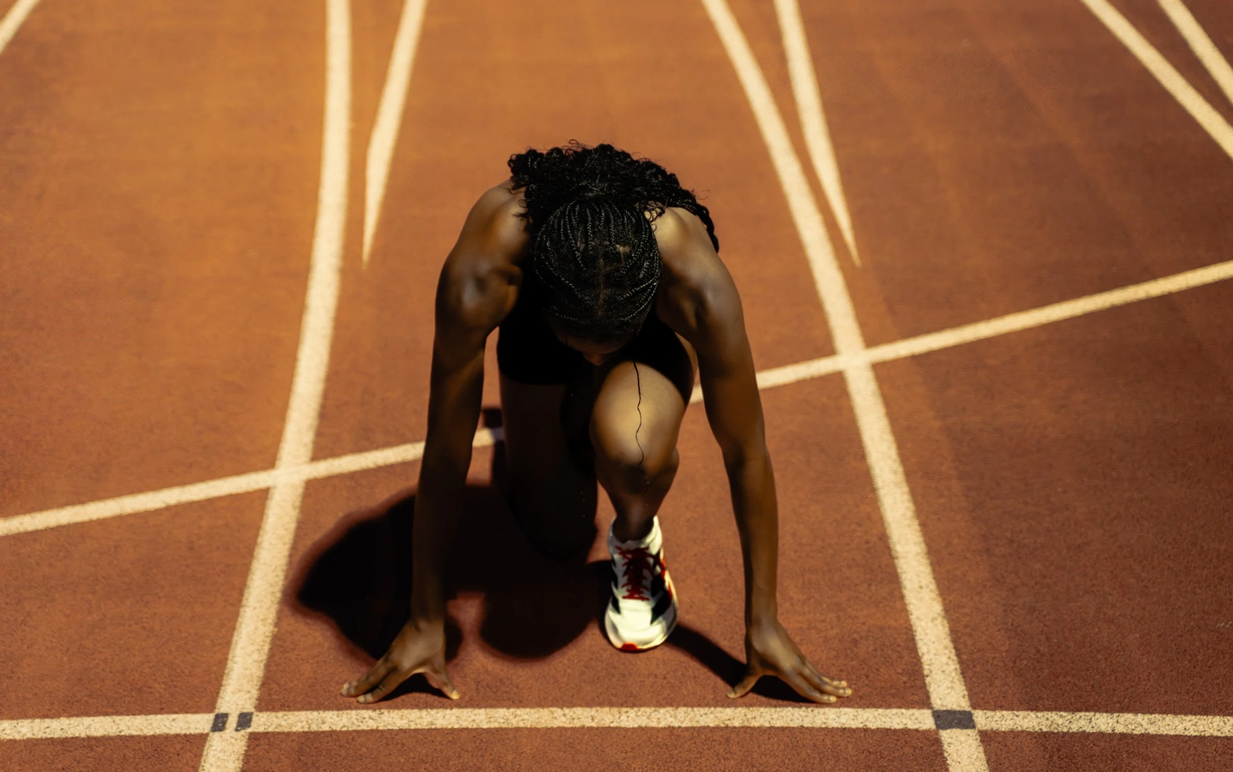 Track athlete crouched at the starting line in Adidas gear, ready for launch — symbolizing preparation and power. Captured at the University of Miami by Stephen Luttinger Photography.