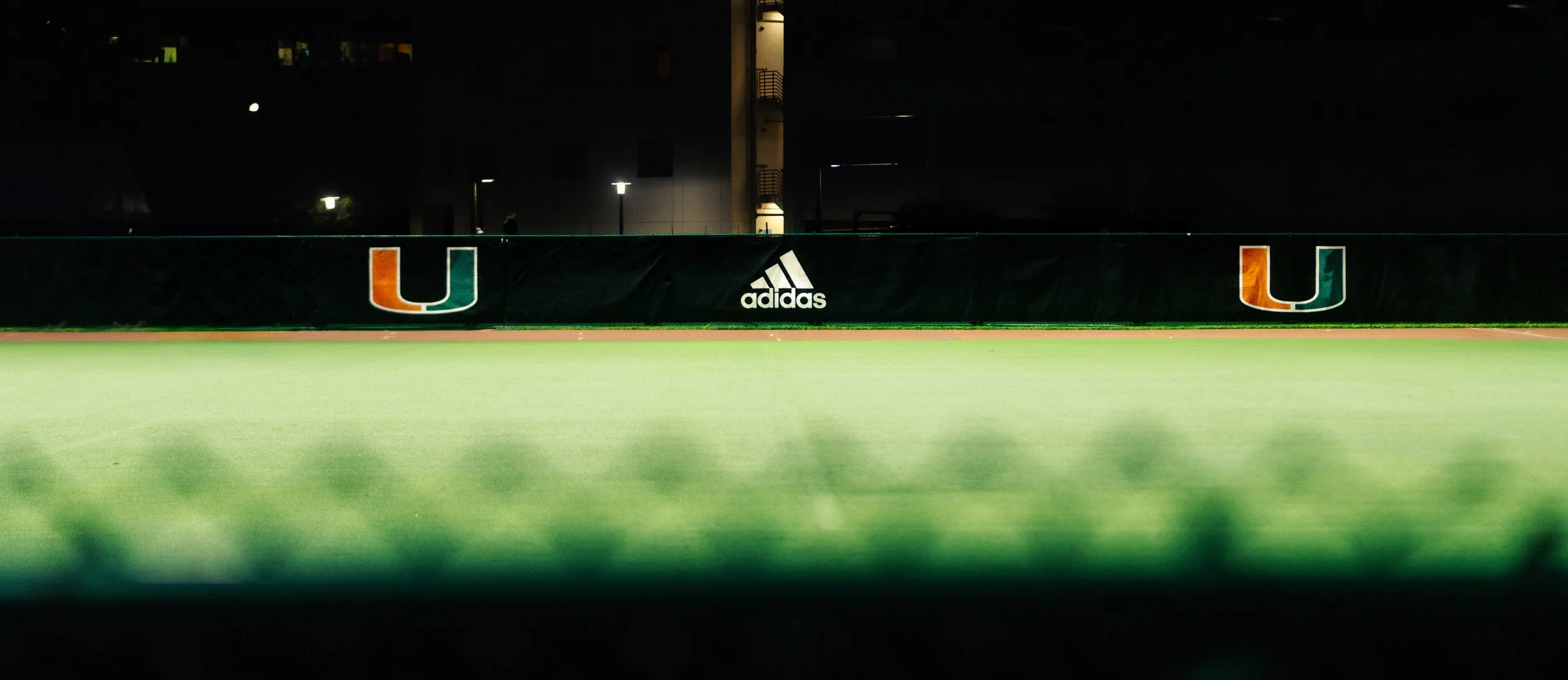 Wide nighttime image of the illuminated Adidas logo across the track fence, symbolizing legacy, consistency, and athletic excellence in South Florida.