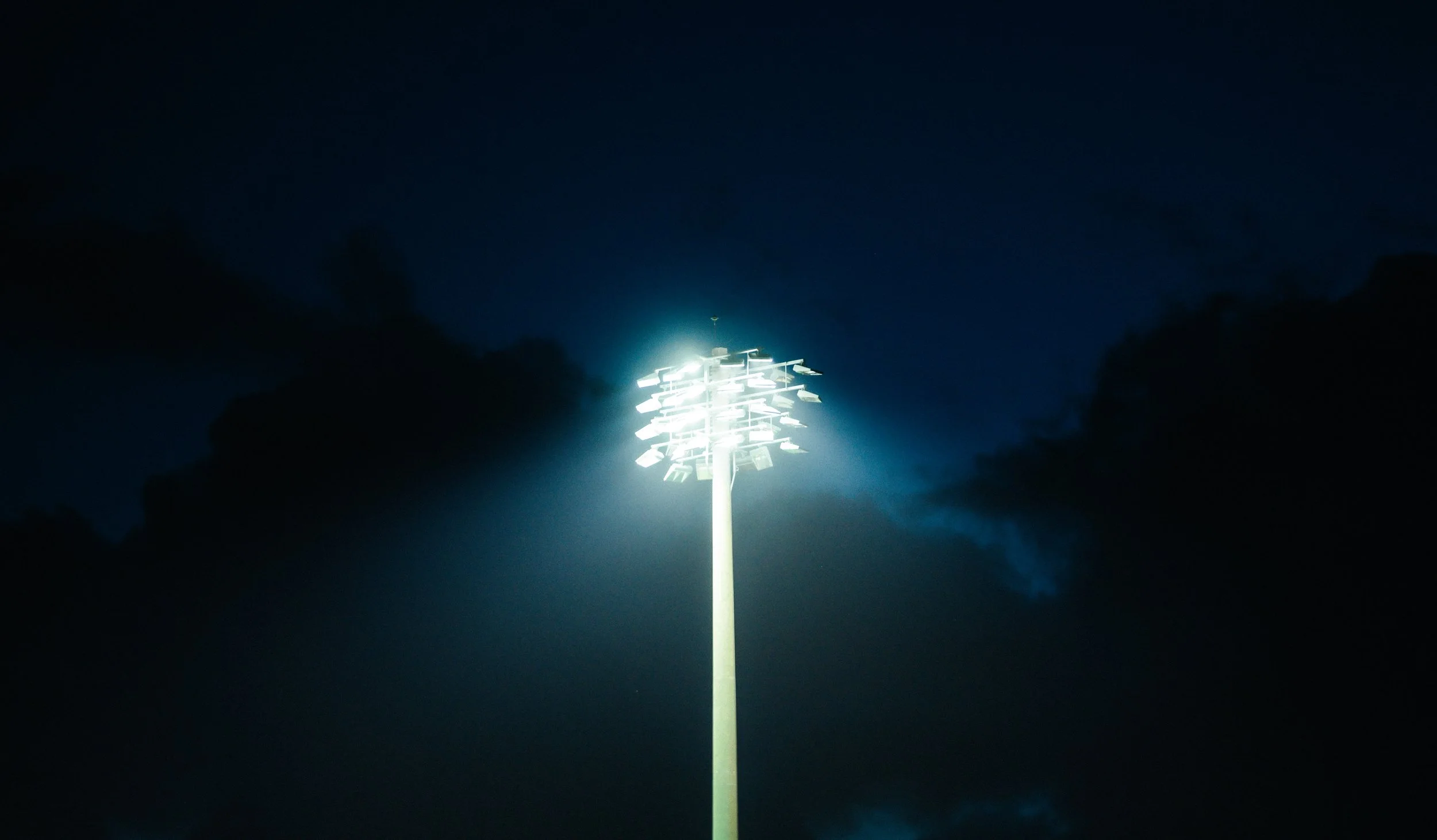 Tall stadium lights glow over the UM track, creating cinematic contrast that anchors Adidas’ dedication to performance under any condition.