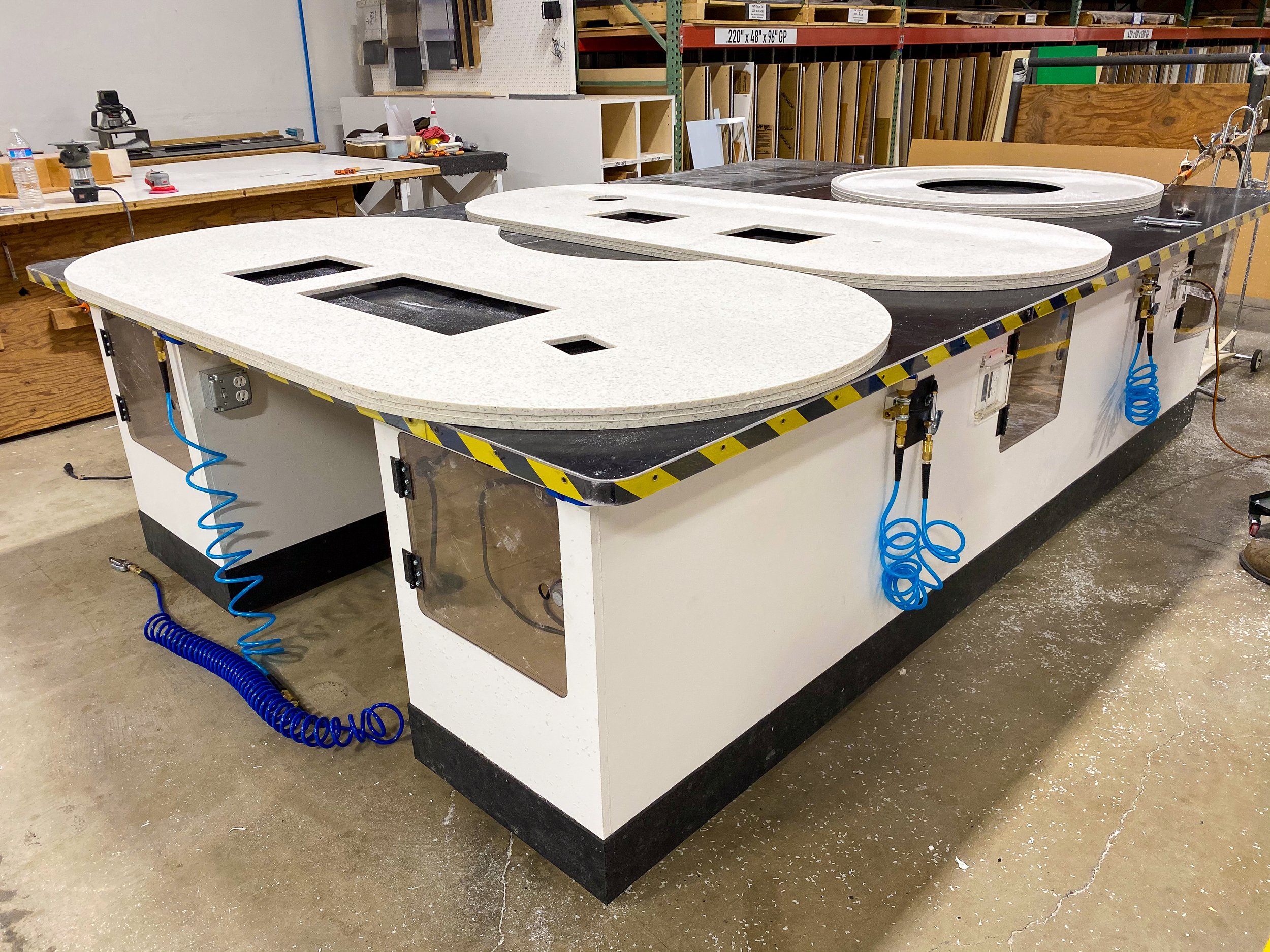 Solid surface plastic table tops with cutouts getting lip detailed glued up in a plastic fabrication facility.