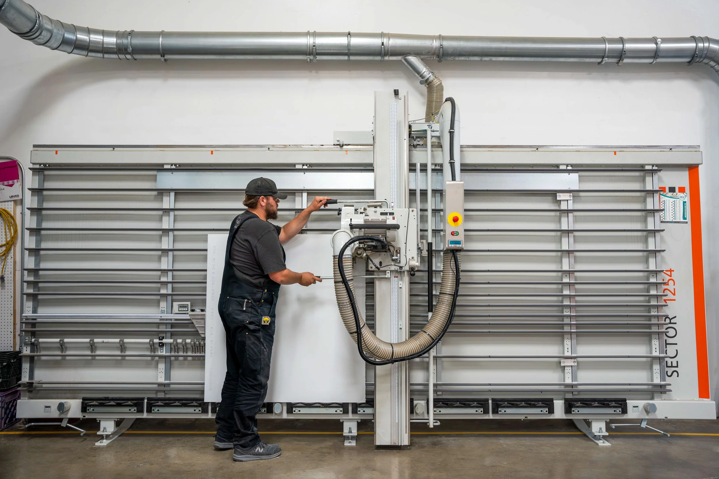 API fabricator using a Holz-Her panel saw with dust collection to cut a sheet of white acrylic.