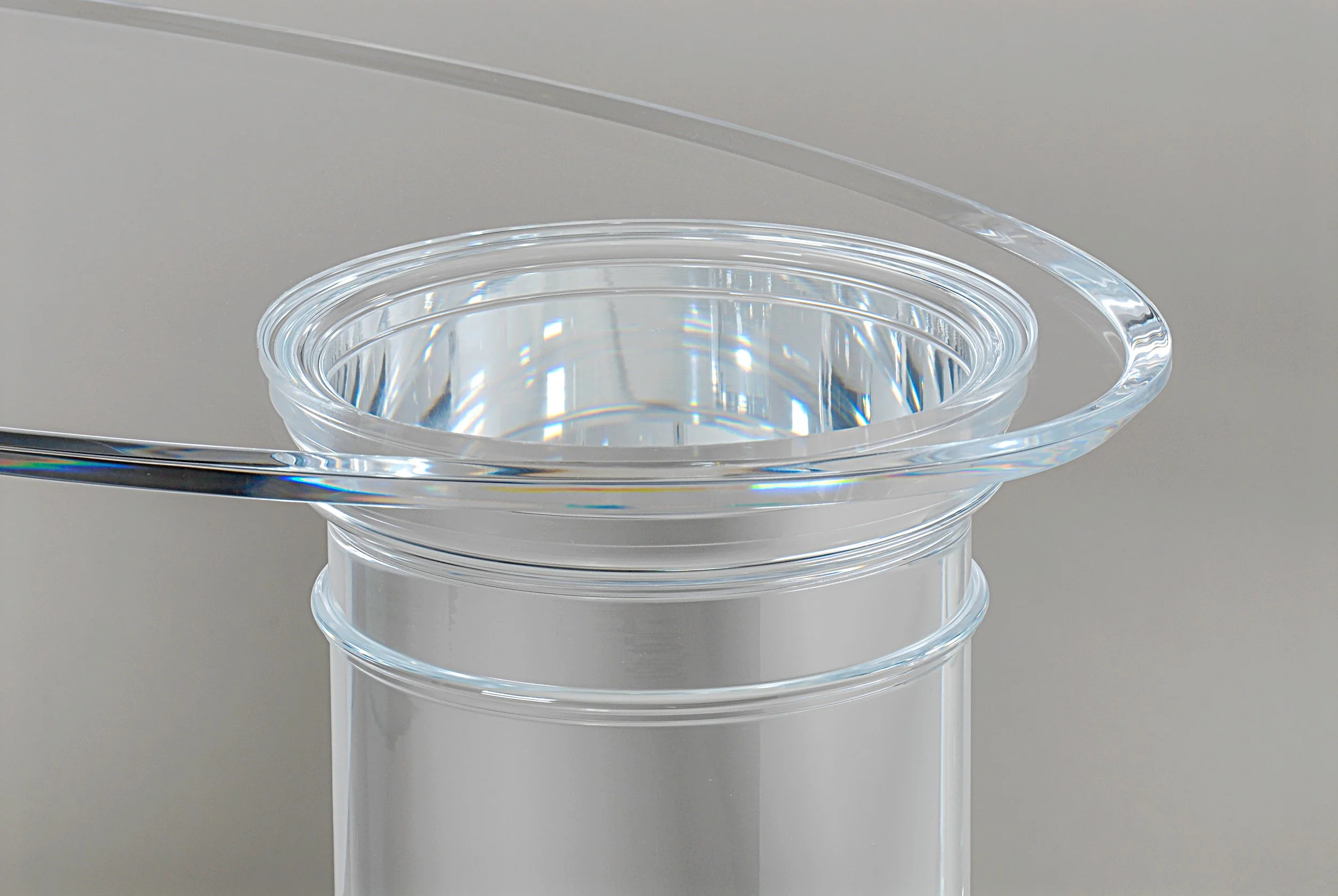 Close up photograph of a clear acrylic oval panel laminated to a clear acrylic cylinder with decorative machining for a table base.