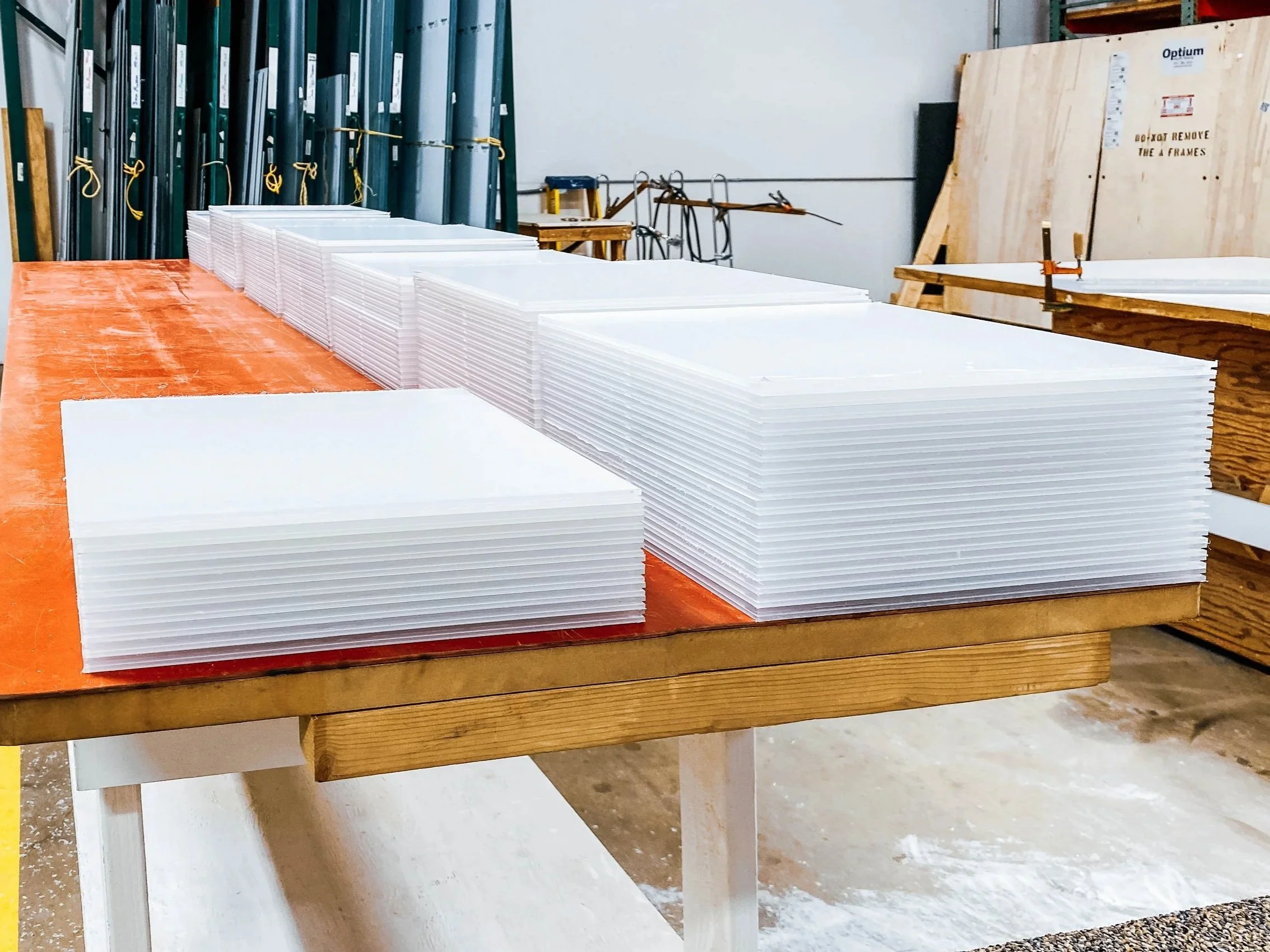 Stacks of precision cut acrylic panels in white masking in a fabrication shop.