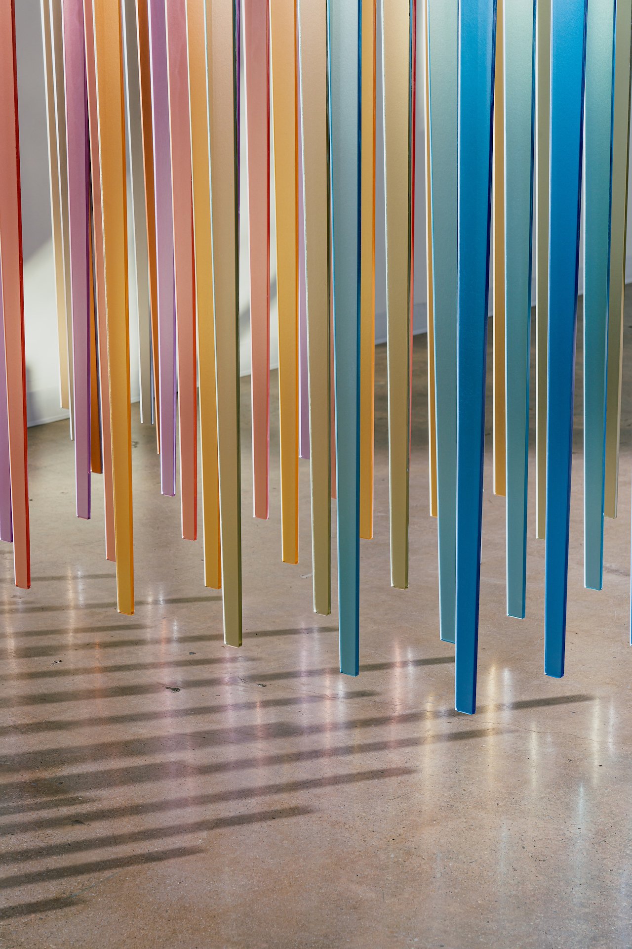 Colorful vertical strips hanging from the ceiling, creating a visual art installation over a polished concrete floor.