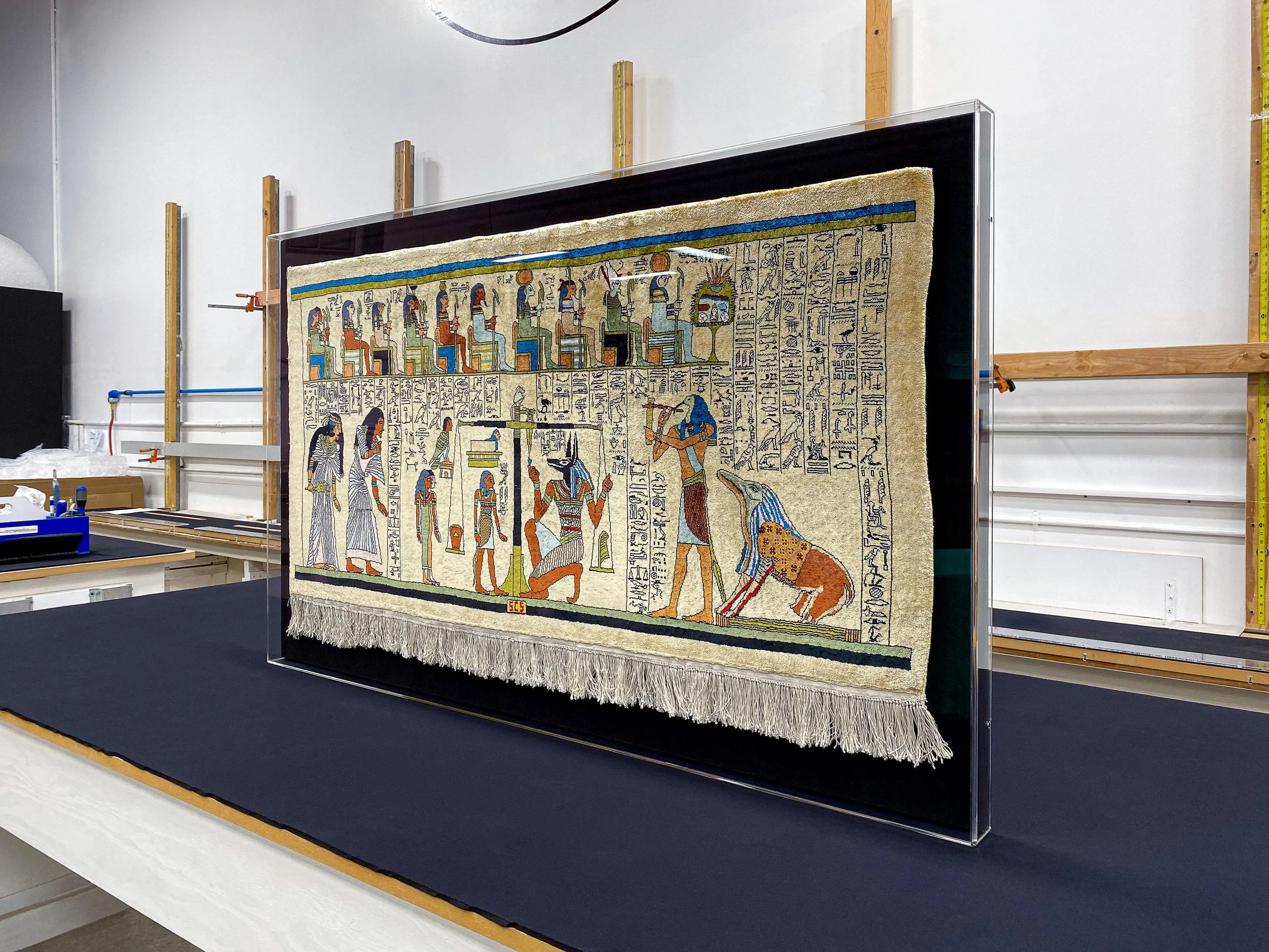 Large acrylic wall-mounted display case designed to protect and present a delicate vintage Egyptian rug mounted to a backer covered in black cloth.