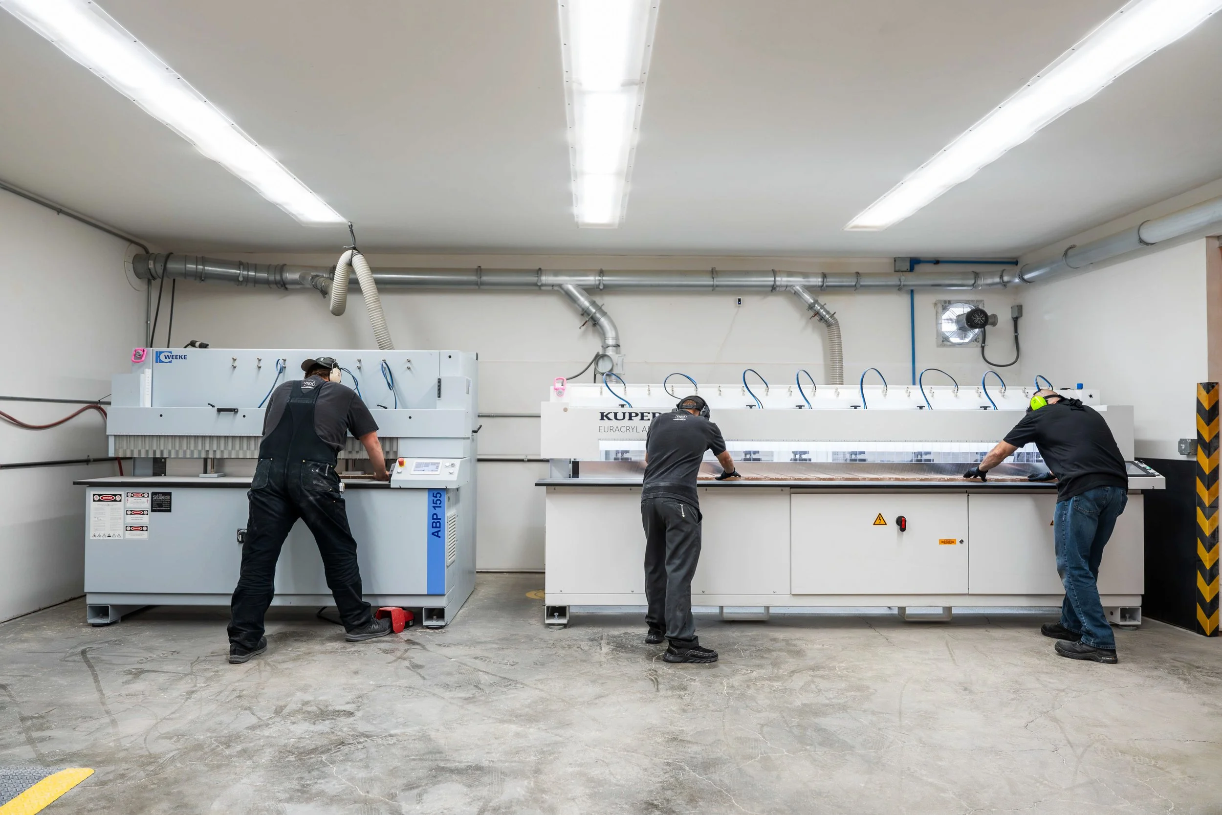 Architectural Plastics, Inc. fabricators at two automated edge polishing machines producing parts during production.