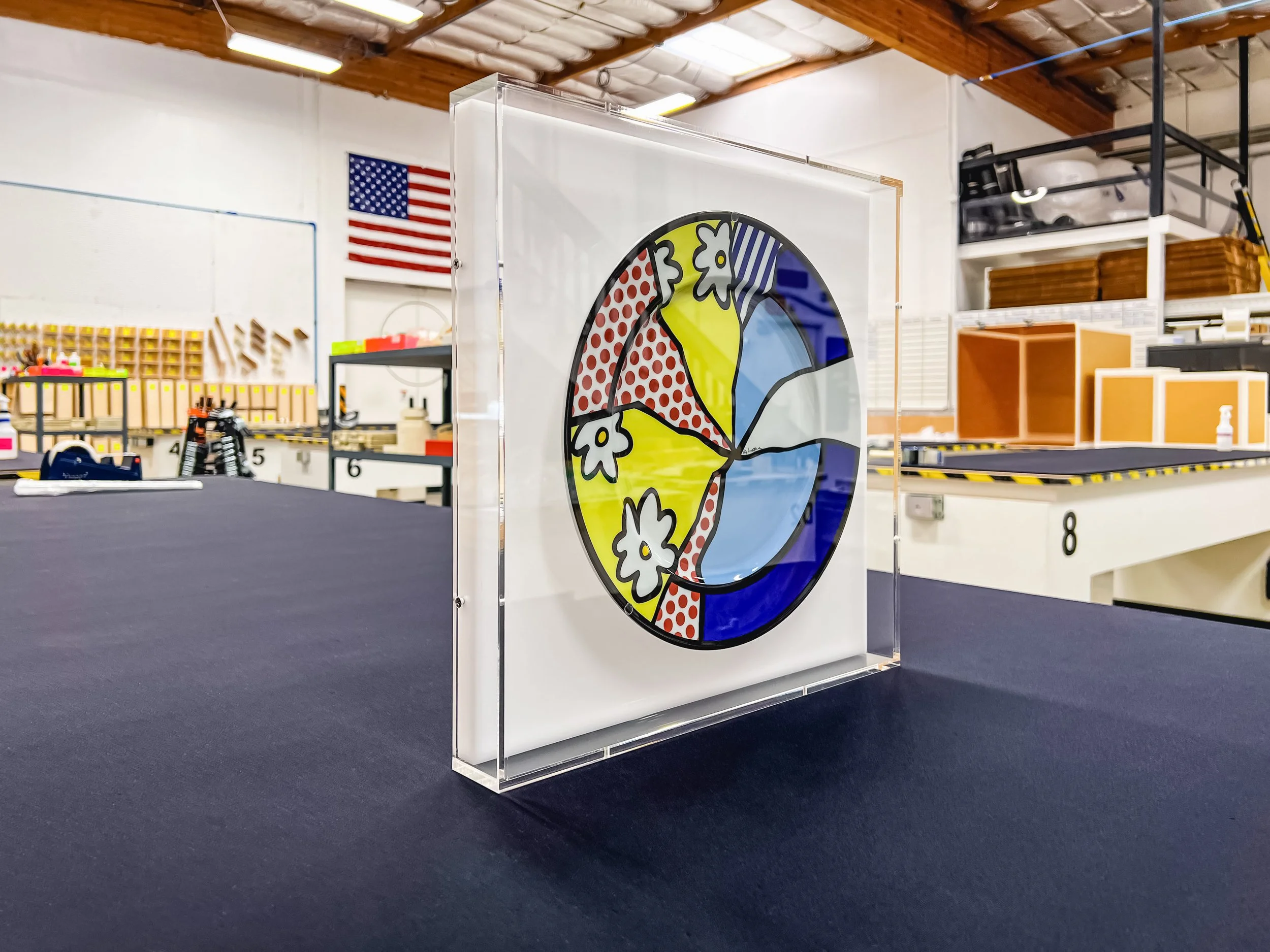 Quality control inspection of a clear acrylic wall-mounted display case protecting a framed Lichtenstein plate.