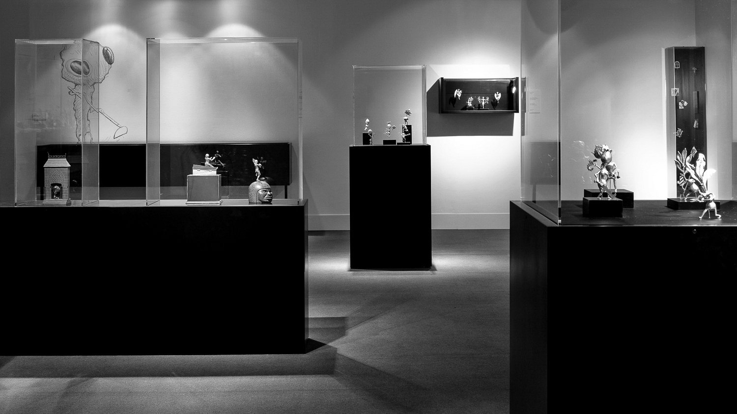 Black and white photo of a museum exhibit with black pedestals, clear acrylic display cases and artifacts.