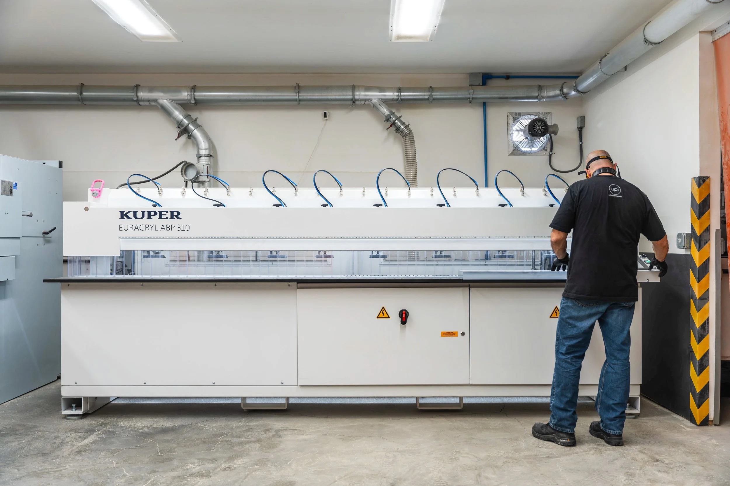 Cnc automated edge polisher in process of polishing a thick slab of clear acrylic, attended by a cnc operator.
