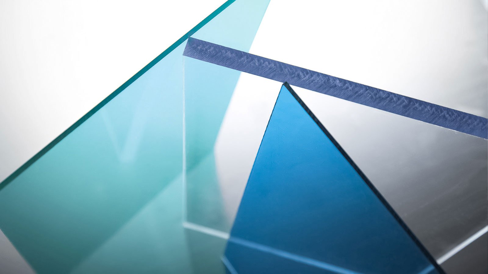 Close-up of geometric glass shapes with reflections and transparent, blue-tinted surfaces.