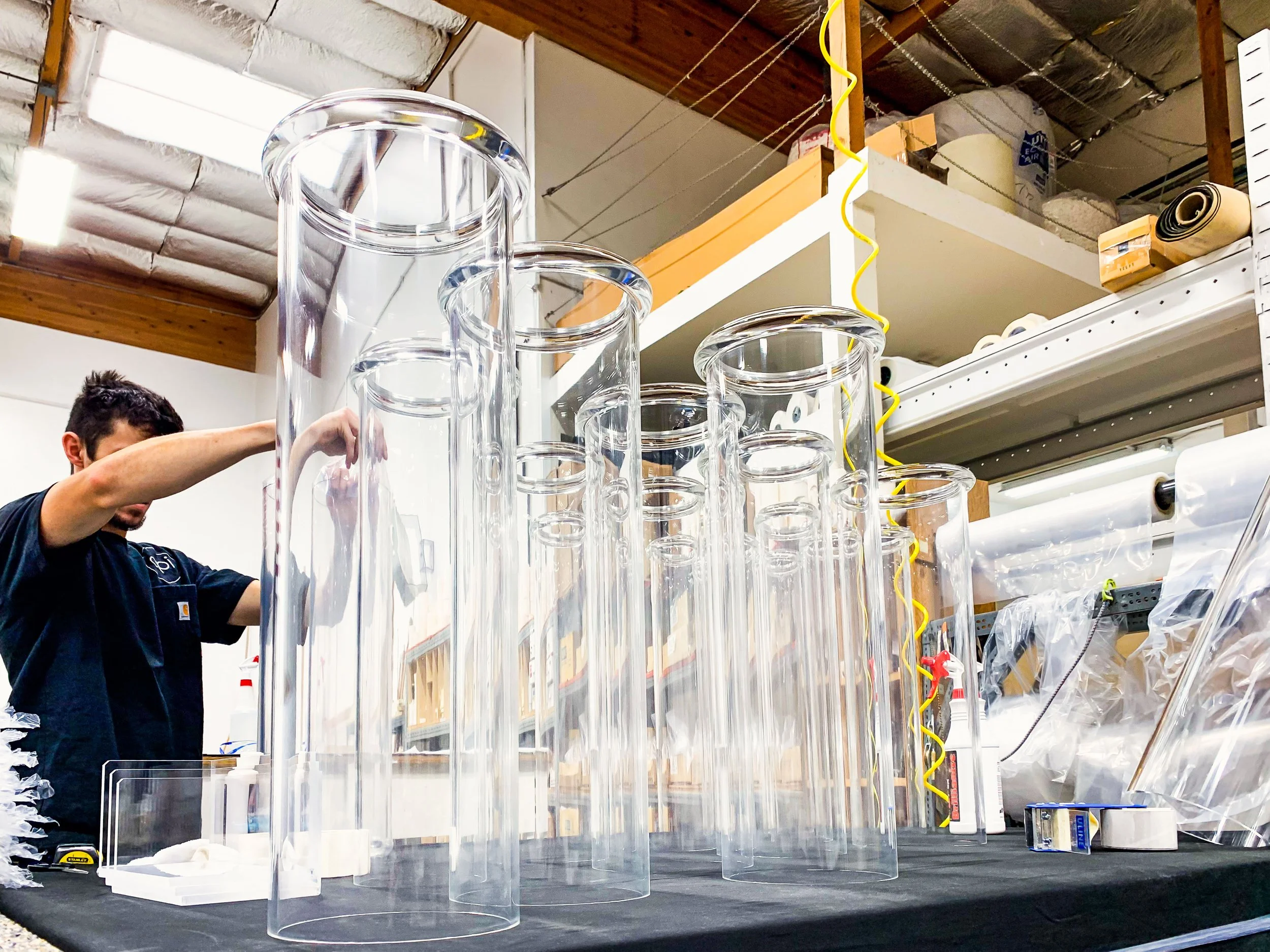 Acrylic fabricator cleaning and wrapping custom acrylic tube assemblies with rounded flanges glued to their tops.