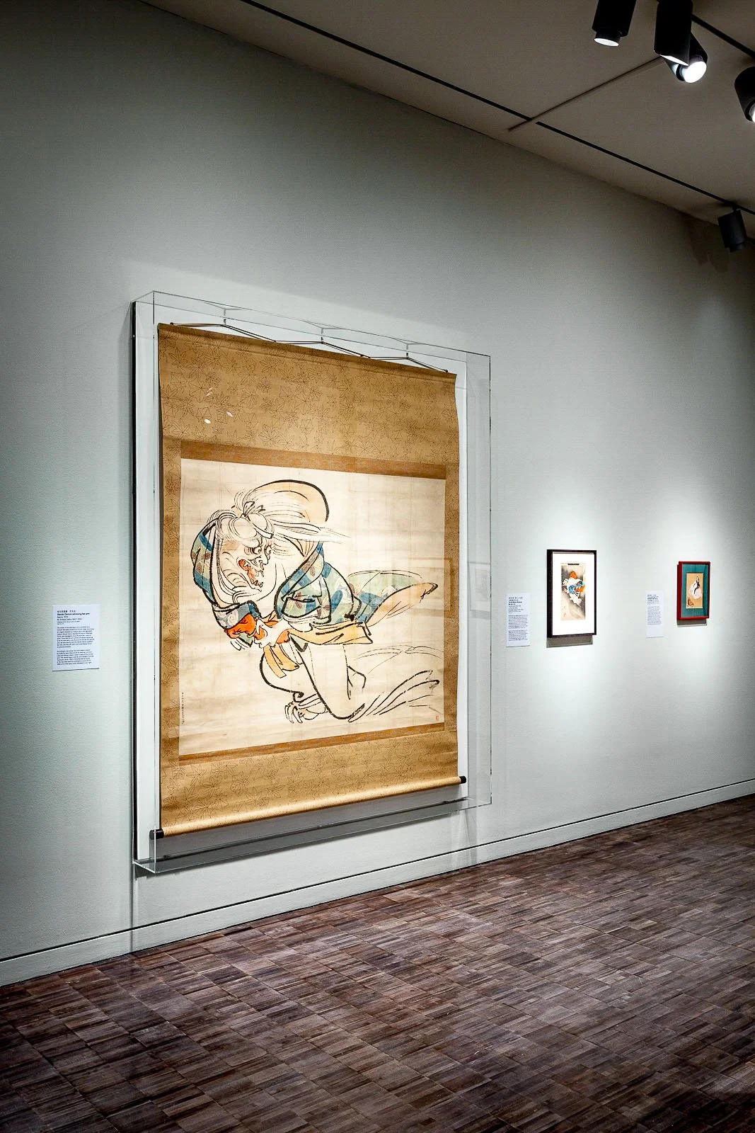 Large wall-mounted acrylic display case protecting a hanging textile artwork in a museum gallery.