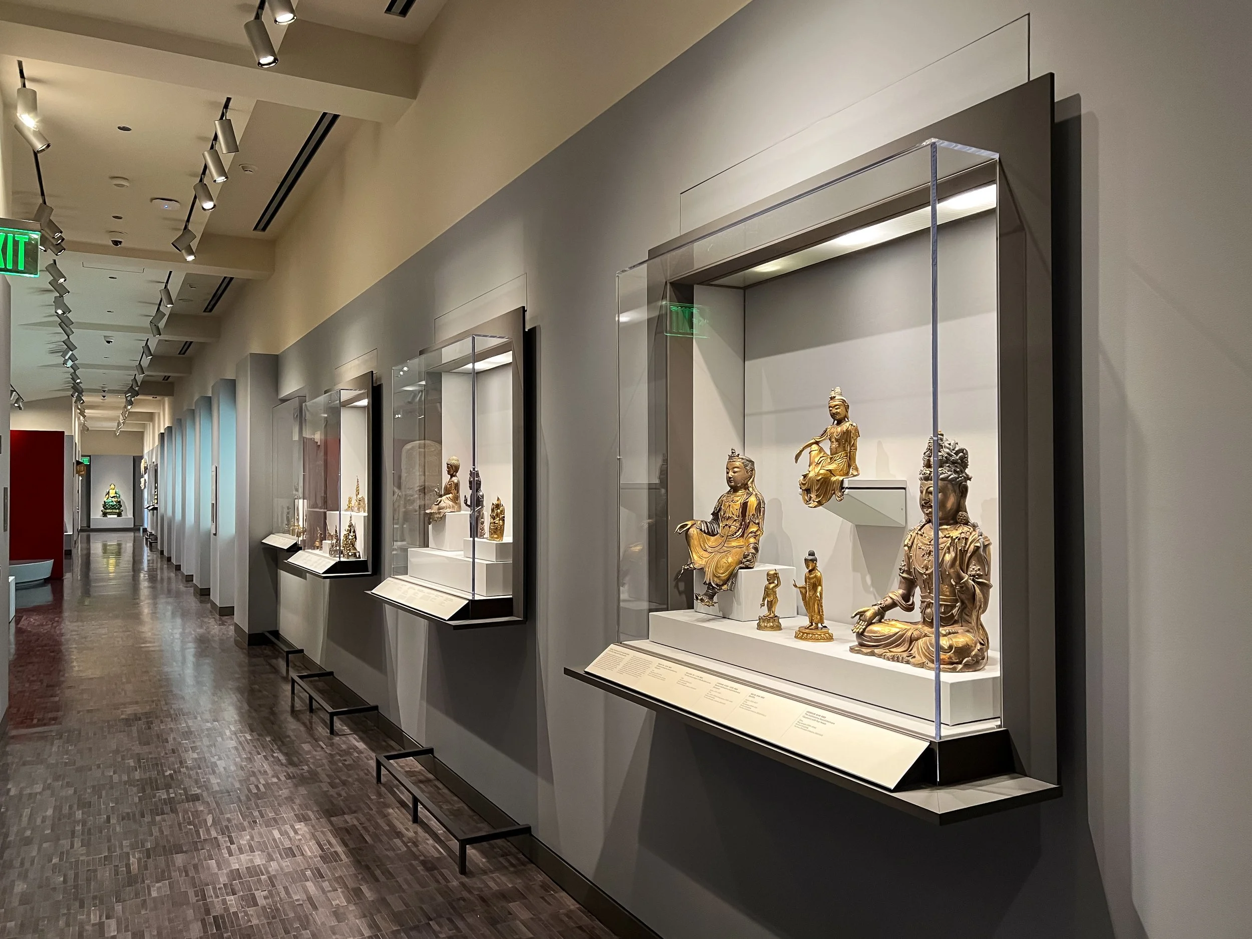 Corridor installation of wall-mounted acrylic vitrine cases displaying objects in a museum exhibit.