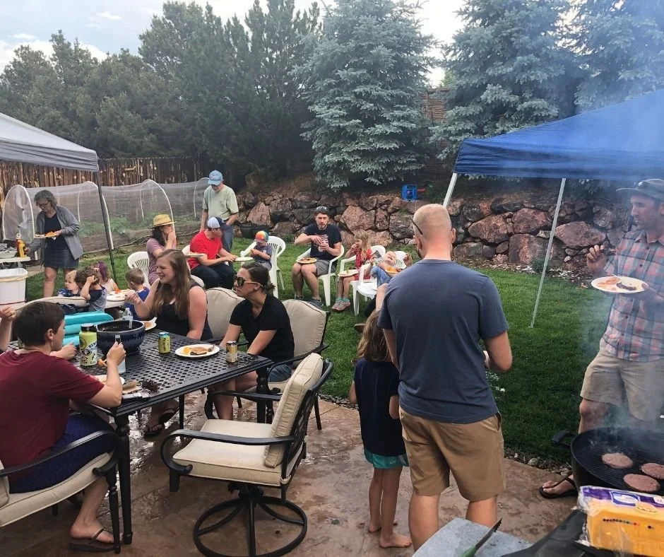 Family and friends enjoying an outdoor backyard gathering with tents, seating, and a grill cooking hamburgers.