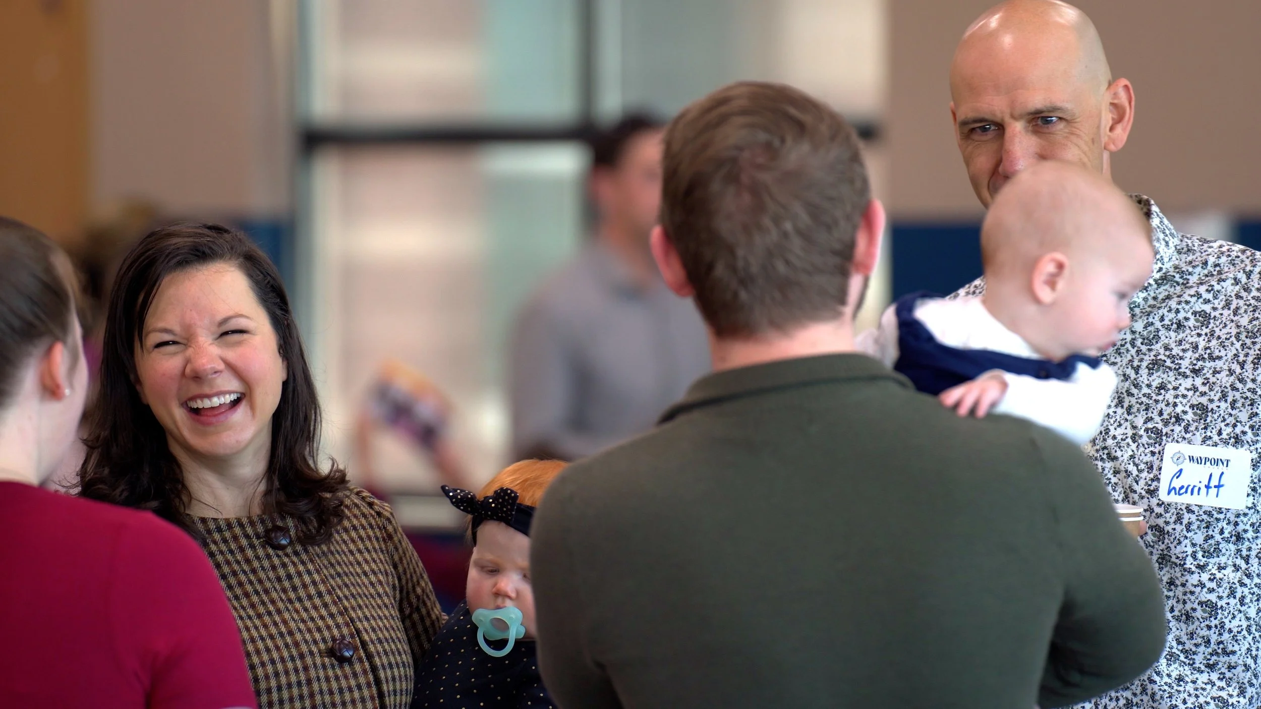 Group of people talking and laughing at an indoor event, some with name tags.