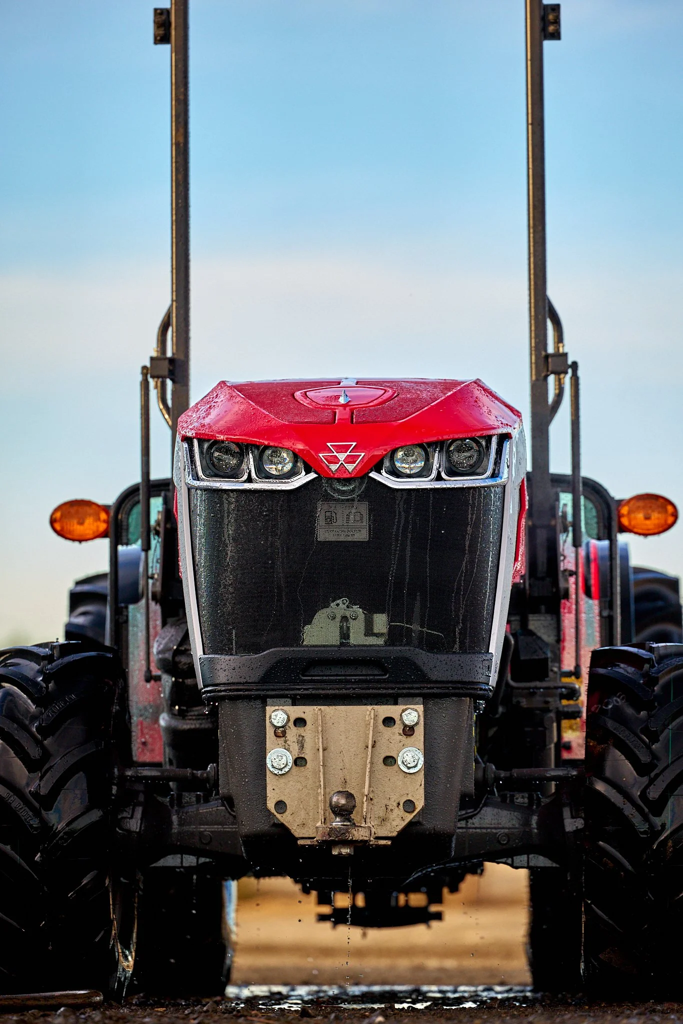 Front view of a red tractor with large black tires, set against a clear sky.