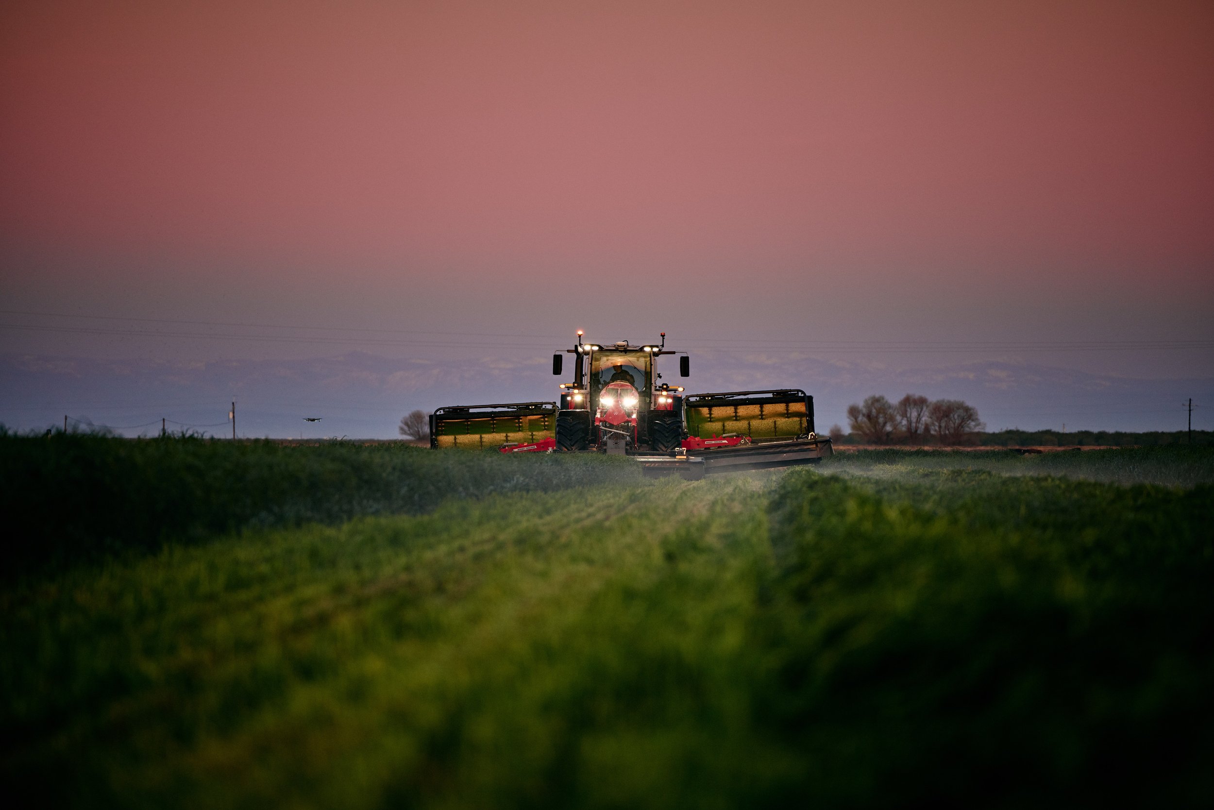 A tractor working in a field at dusk or dawn with a pinkish sky in the background.