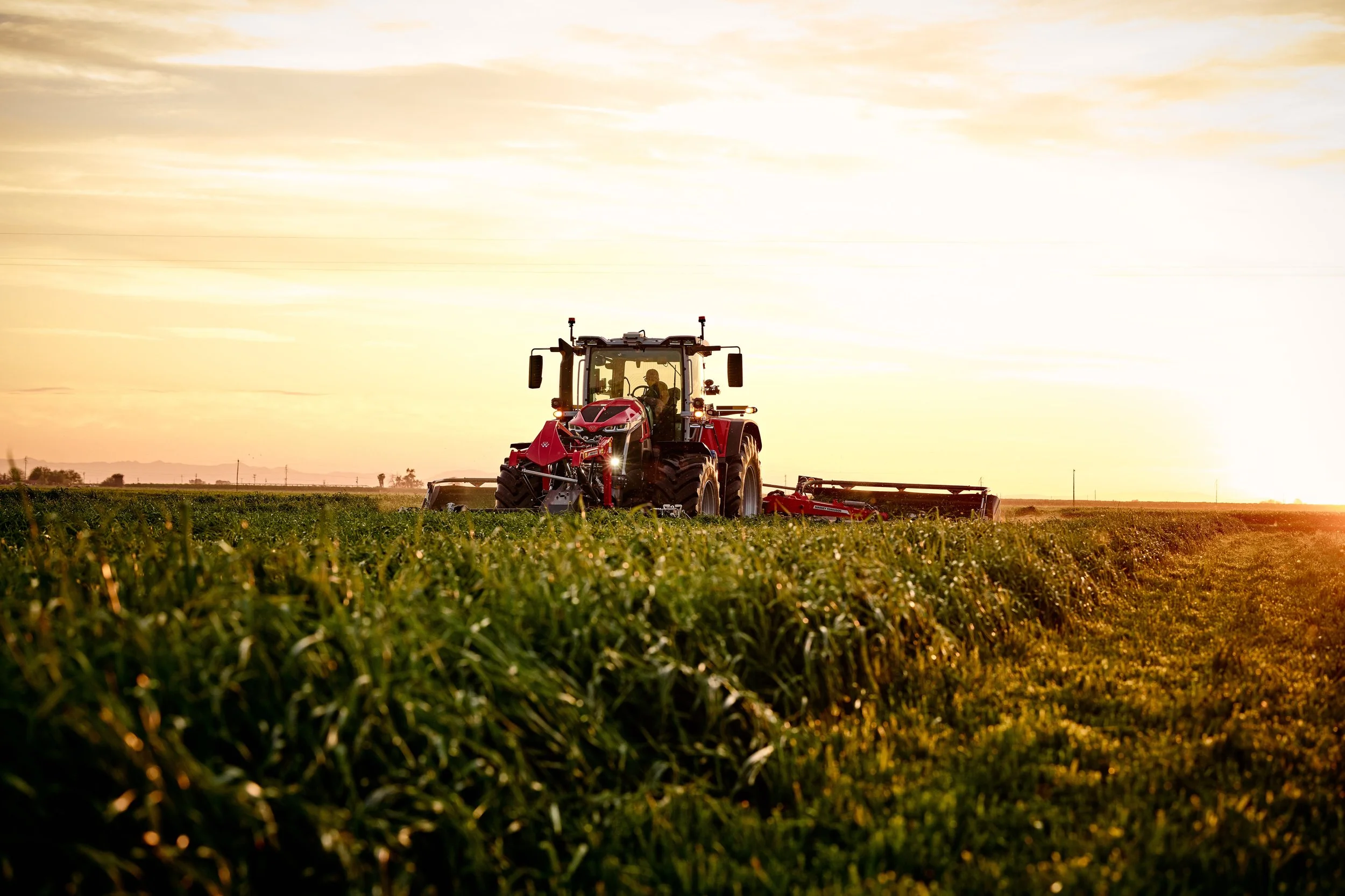 A red tractor working on a green field at sunset.